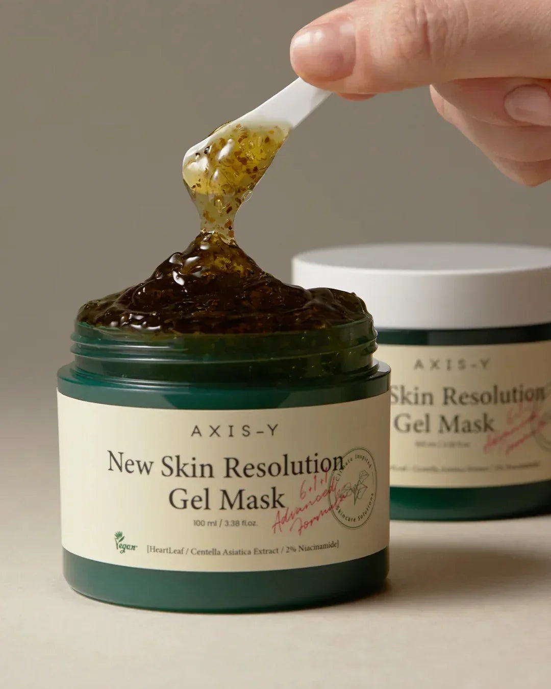 Open jar of Axis-Y New Skin Resolution Gel Mask with gel scoop held above it showing texture
