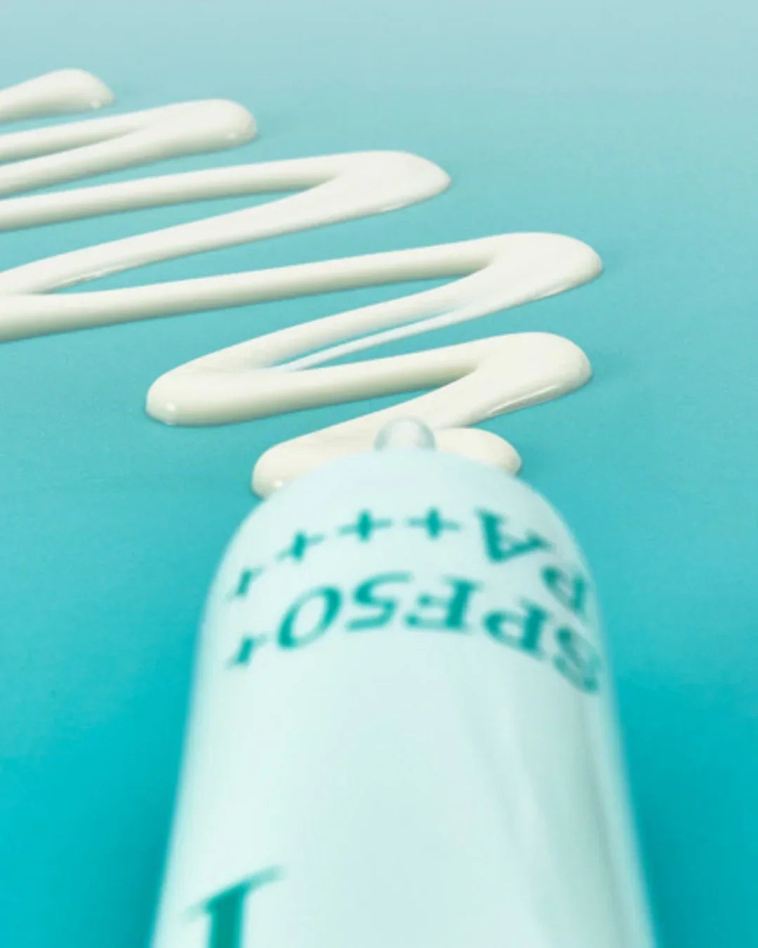 Close-up of white sunscreen cream zigzag applied on turquoise surface with blurred SPF50 tube