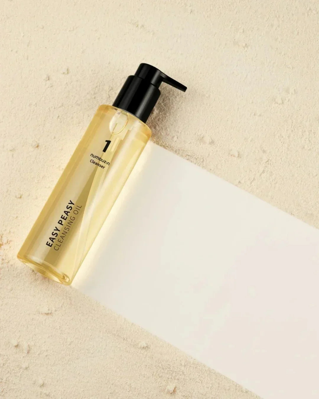 Easy Peasy Cleansing Oil bottle with black pump on beige textured surface with white paper