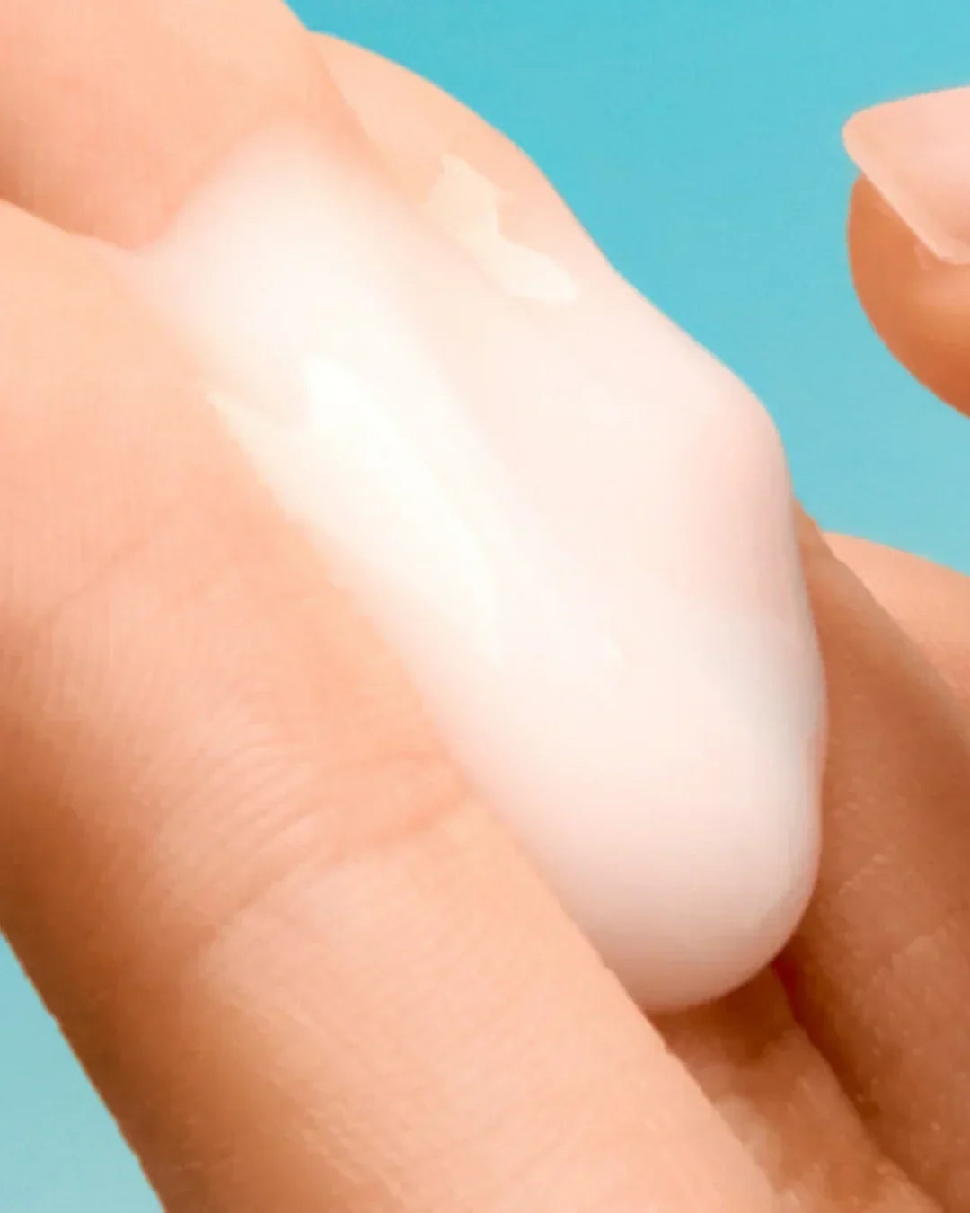 Close-up of creamy white soothing cream on fingers with blue background