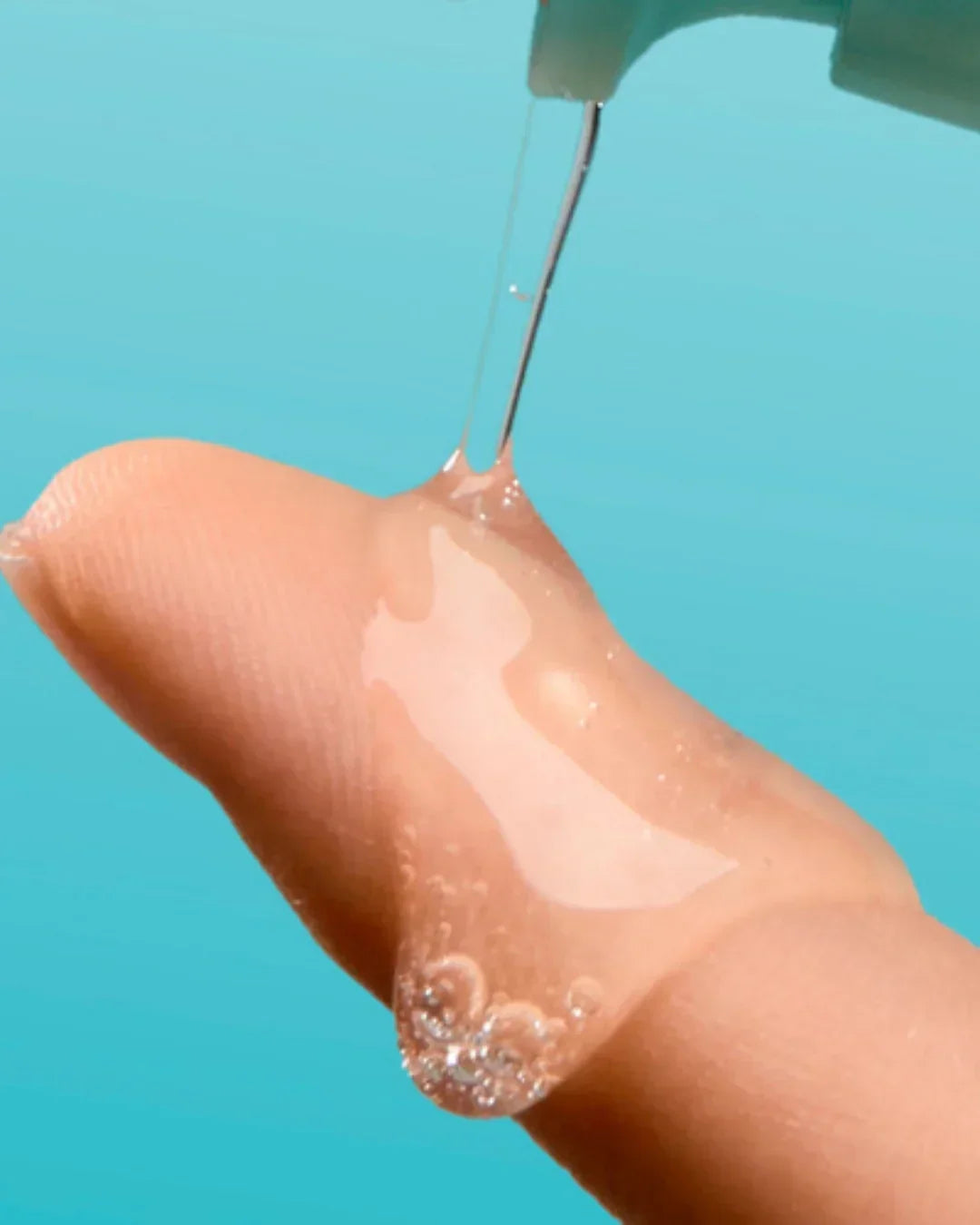 Clear soothing serum applied on fingertip with blue background, showing gel texture and bubbles