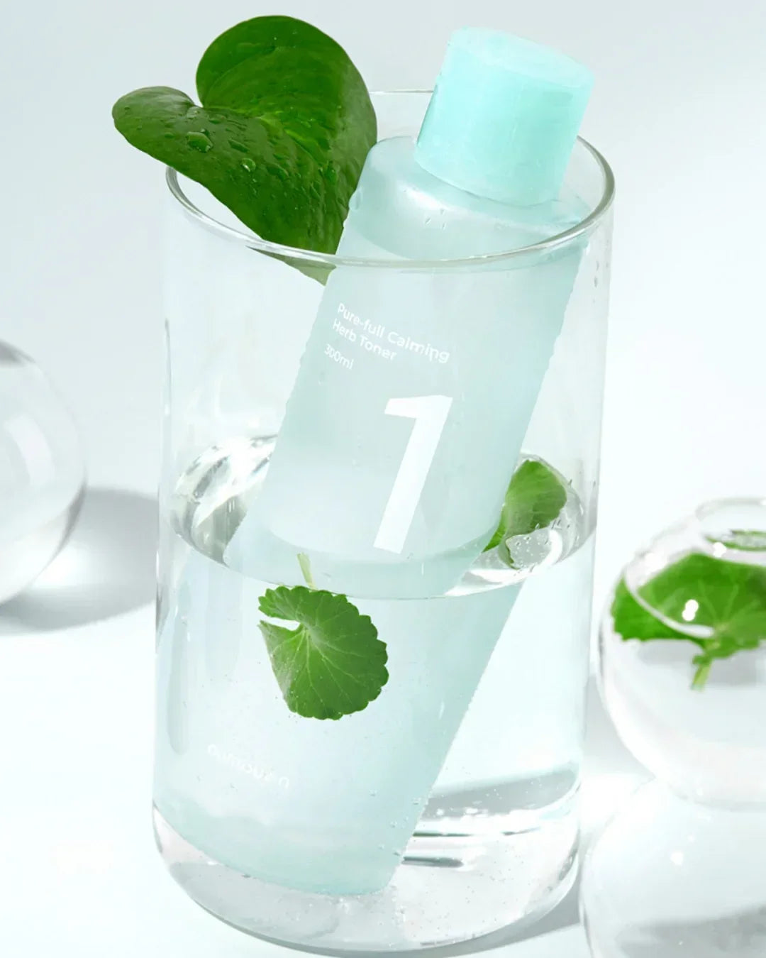 Clear bottle of Pure.full Calming Herb Toner with blue cap submerged in water with green leaves