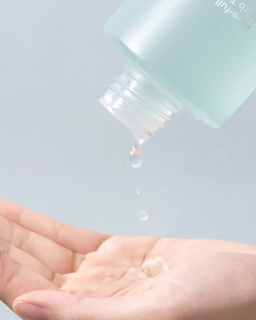 Hand catching clear calming toner drops flowing from a light blue skincare bottle