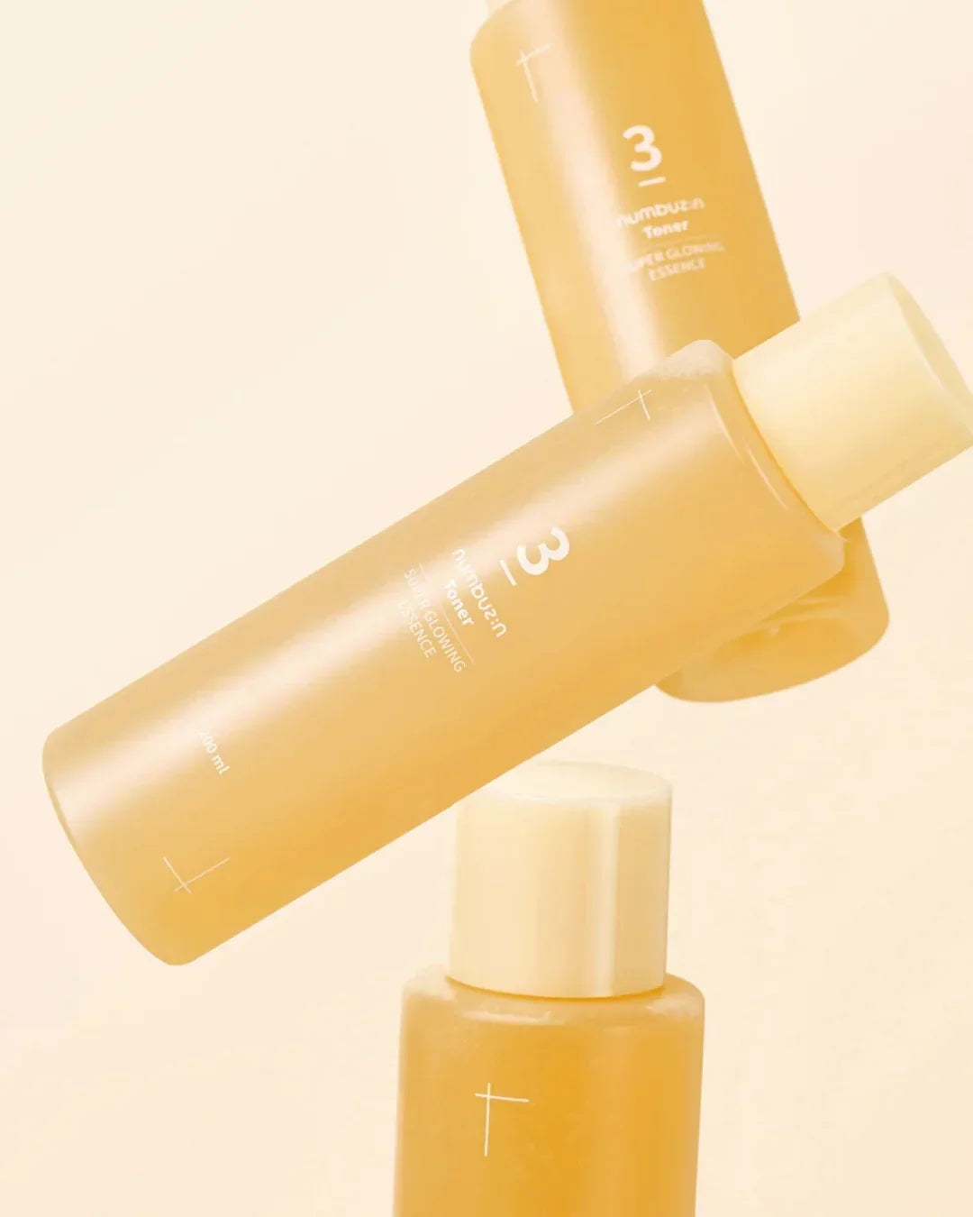 Three yellow Numbuzin No3 Super Glowing Essence Toner bottles in soft lighting backdrop