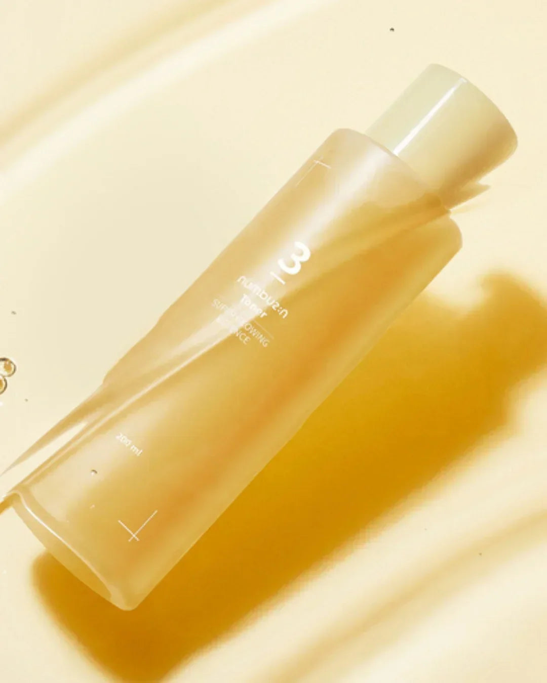 No3 Super Glowing Essence Toner 200ml bottle with golden liquid texture on yellow background