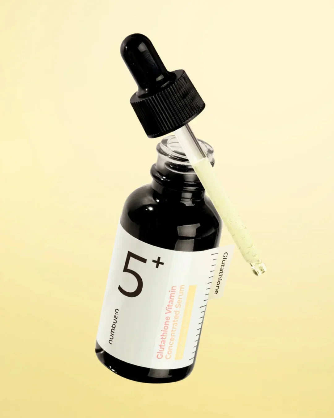 Glass dropper bottle of 5+ Glutathione Vitamin Concentrated Serum with visible serum drop, beige background