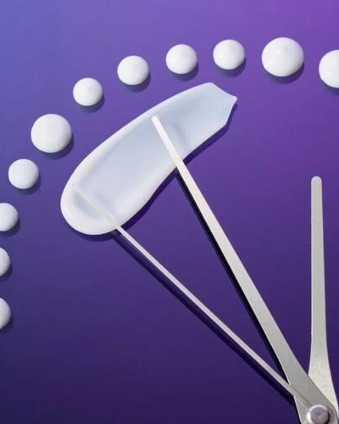Close-up of white skincare cream dots arranged like a clock with metal clock hands on purple background