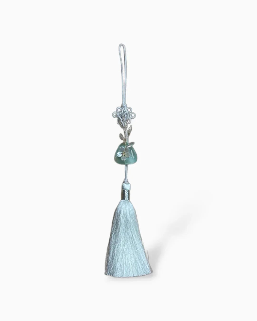 white norigae tassel with blue jade ornament and delicate floral detail on white background