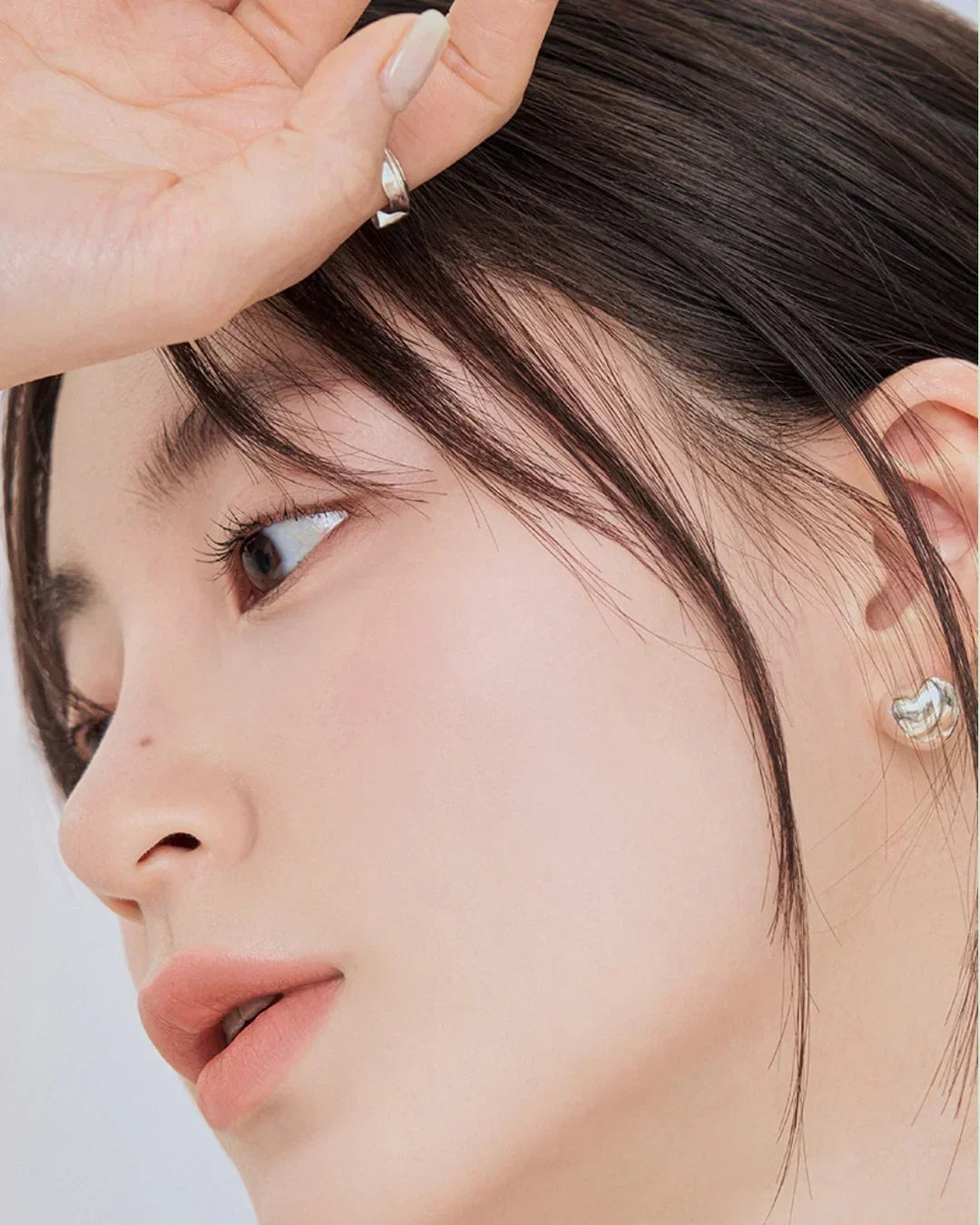 Close-up of a woman with smooth skin, natural makeup, silver earrings, and manicured nails