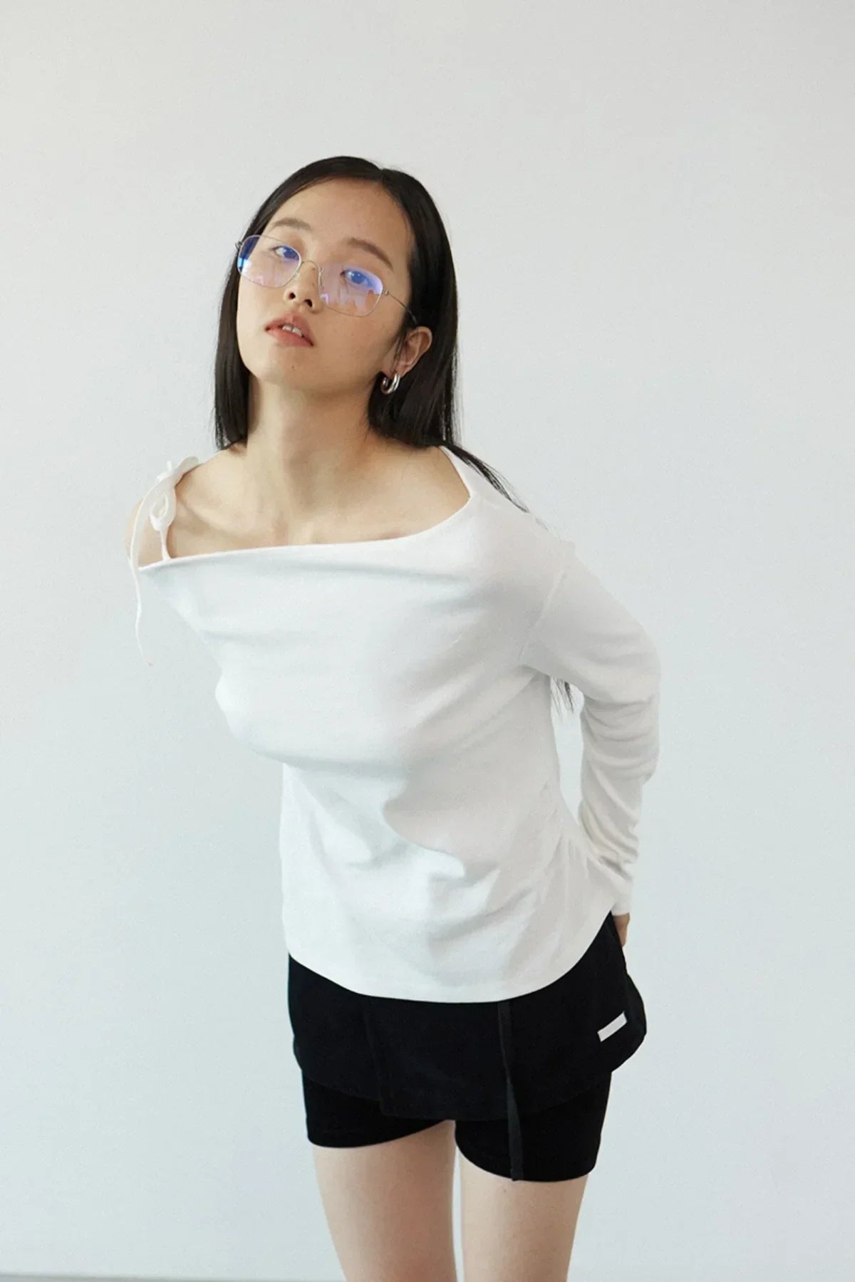 Woman wearing ivory off-shoulder long sleeve top and black shorts posing against white background