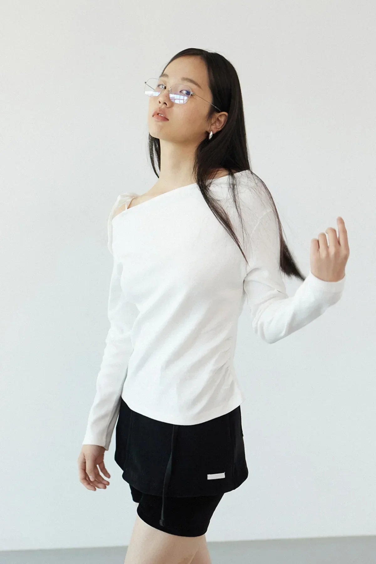 Woman wearing off-shoulder ivory long-sleeve top and black skirt against white background