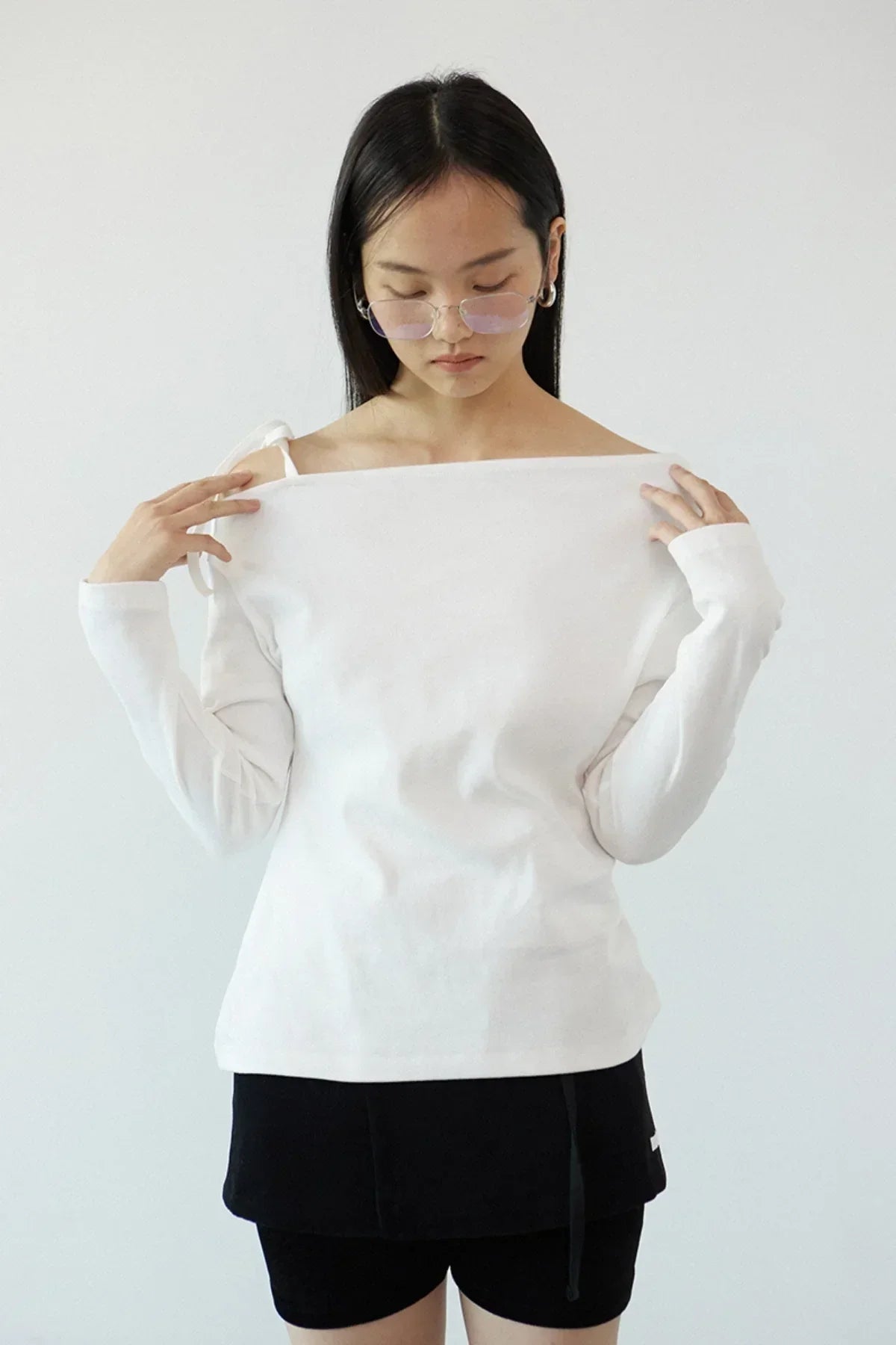 Woman wearing off-shoulder long sleeves ivory top with black shorts and pink tinted glasses