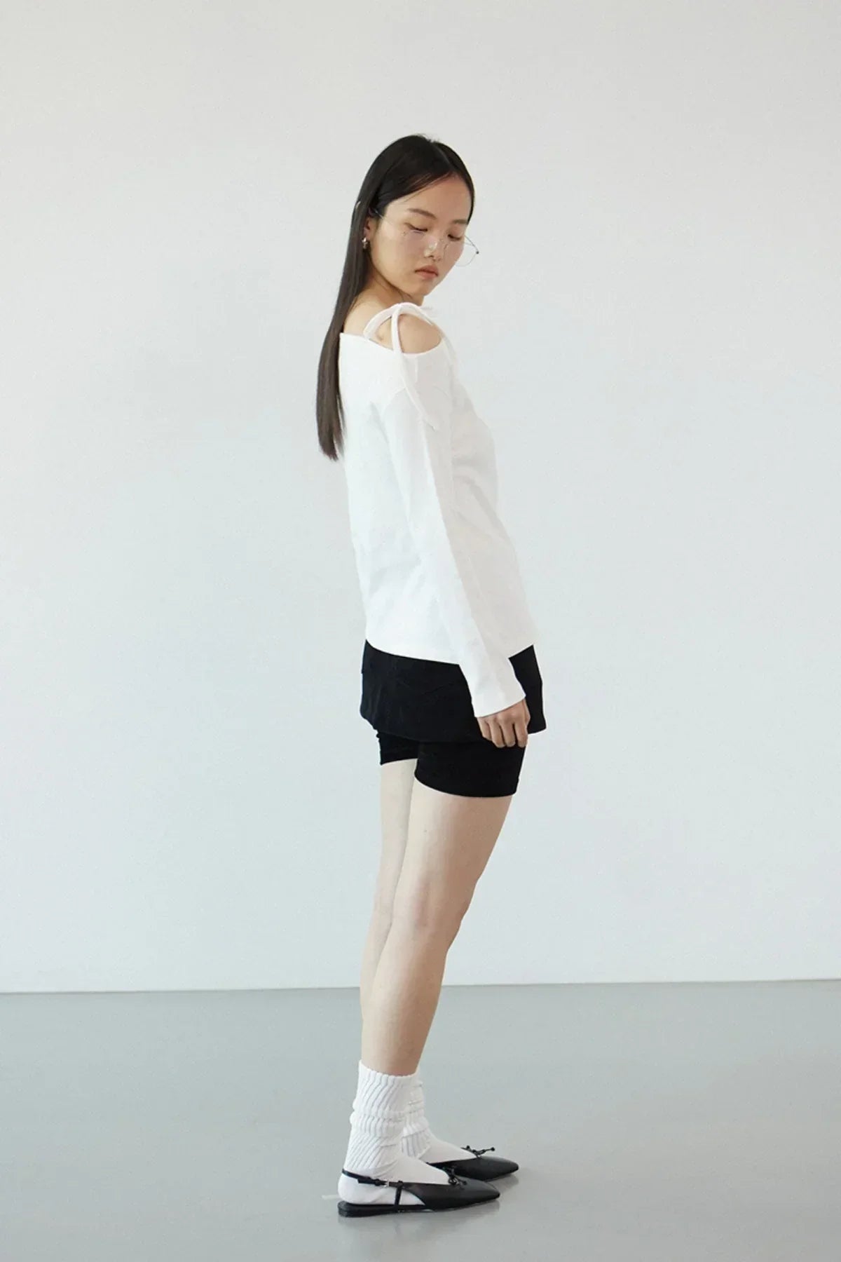 Model wearing ivory off-shoulder long sleeve top with black shorts and white socks in minimalist setting