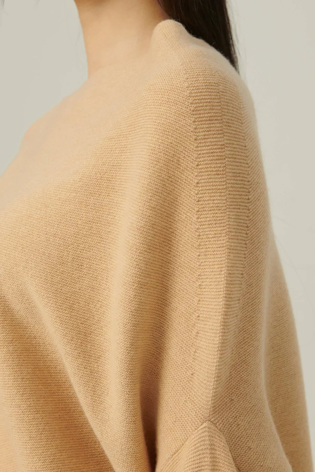 Close-up of beige one-shoulder flow knit top on model with textured stitching detail