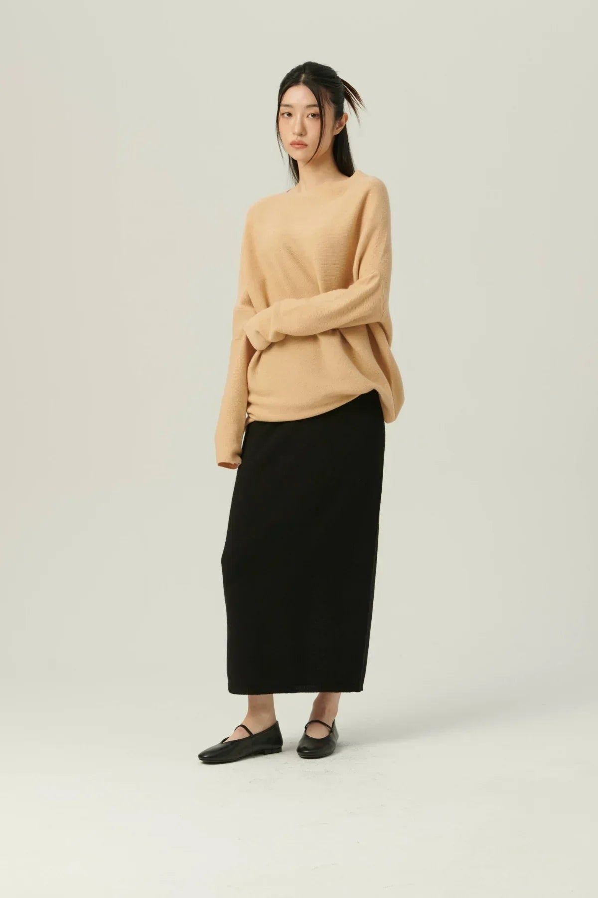 Woman wearing beige oversized knit sweater with black midi skirt and black flats in studio