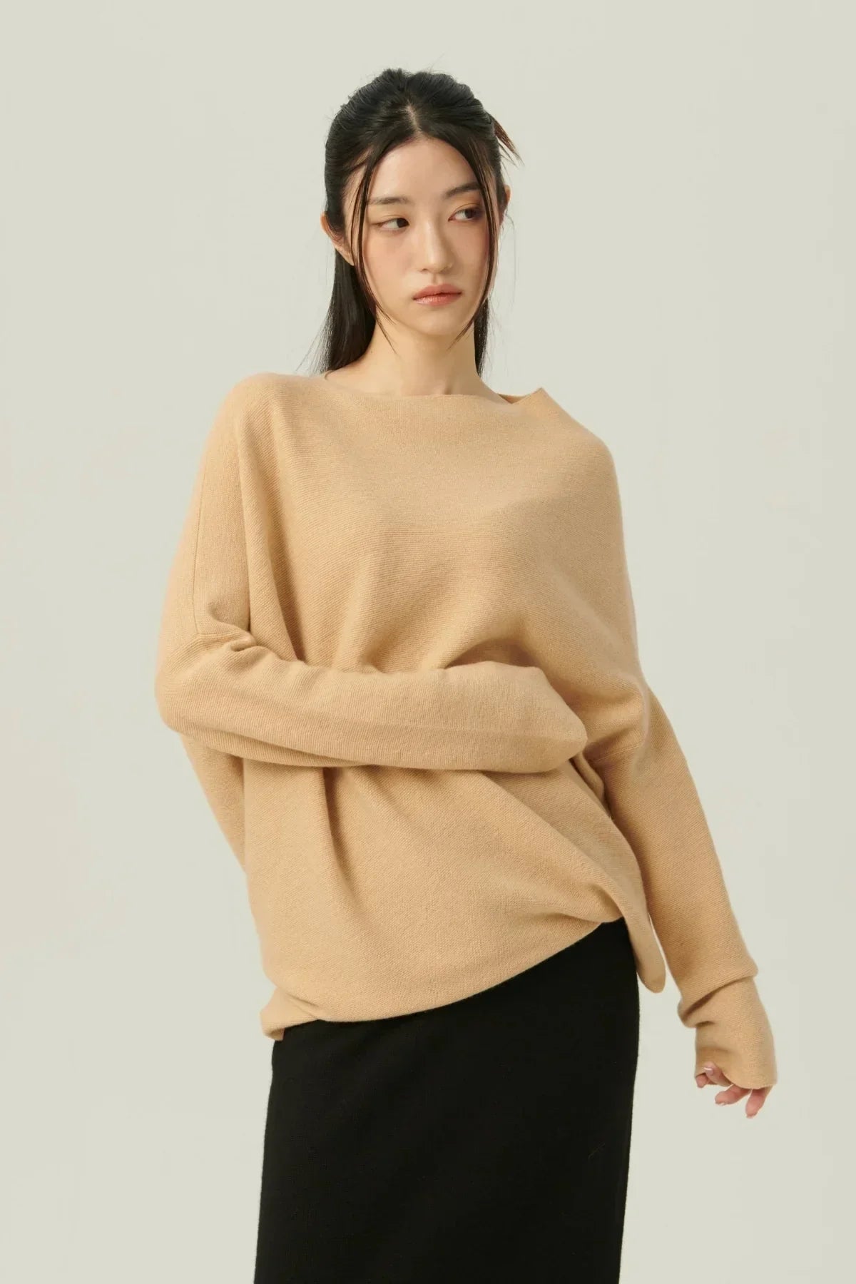 Woman wearing beige oversized knit sweater with long sleeves and black skirt against light background