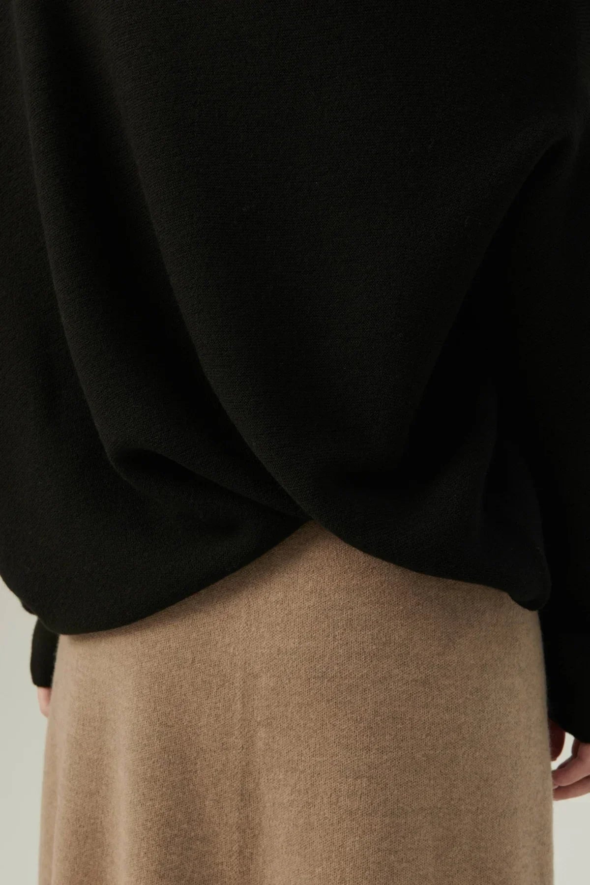 Close-up of black flow knit top draped over beige knit skirt, showcasing texture and fabric details