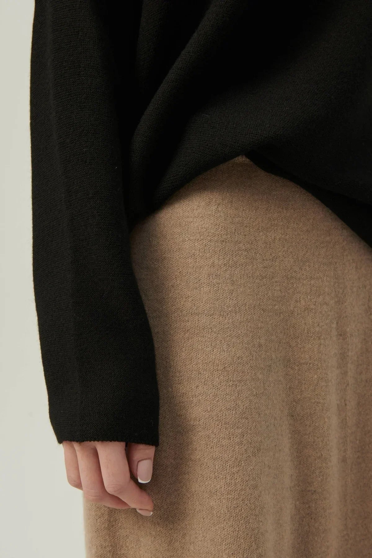 Close-up of a person wearing a black long sleeve knit top and beige knit skirt with French manicure