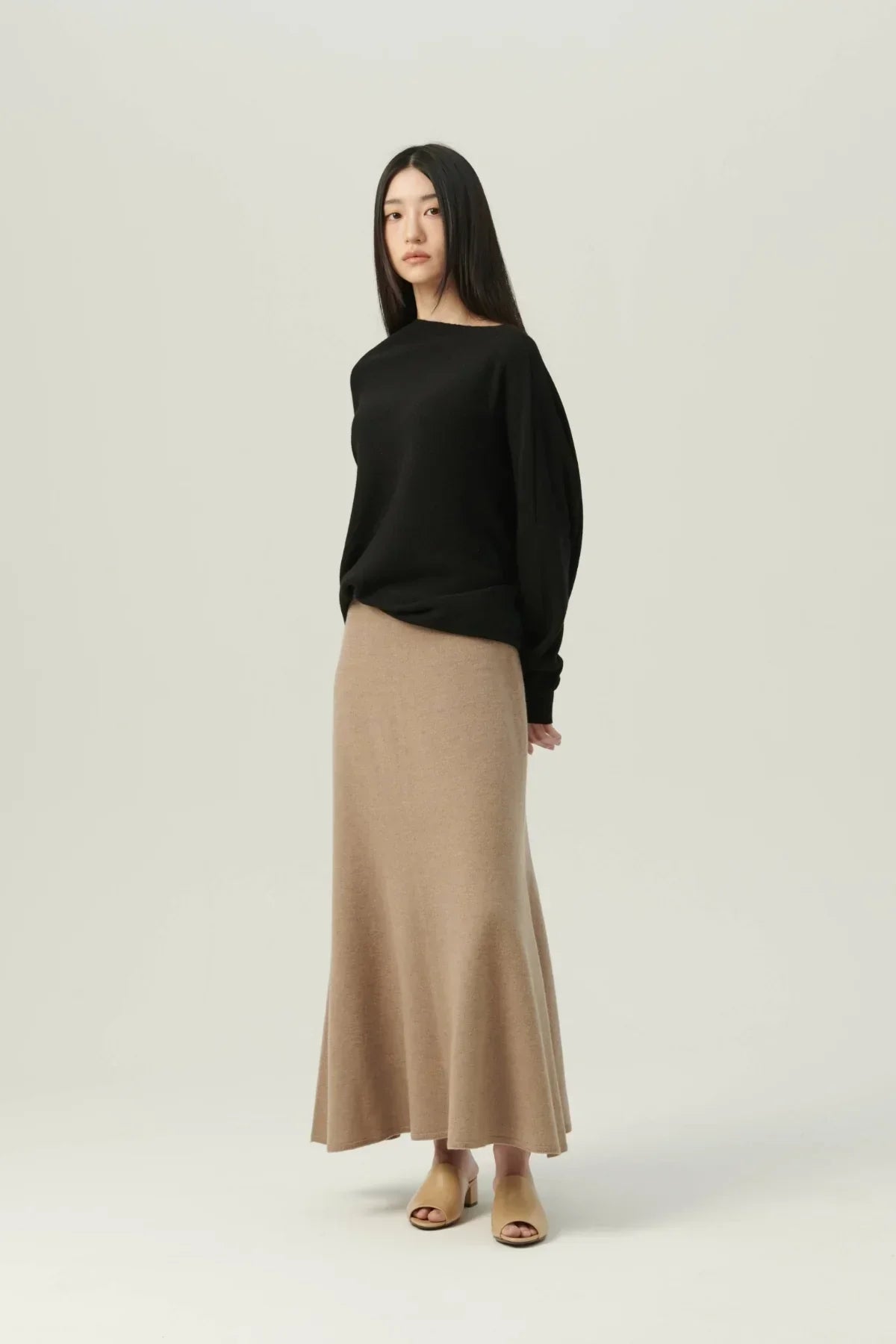 Woman wearing black oversized knit sweater and beige long skirt with tan open-toe heels on light background