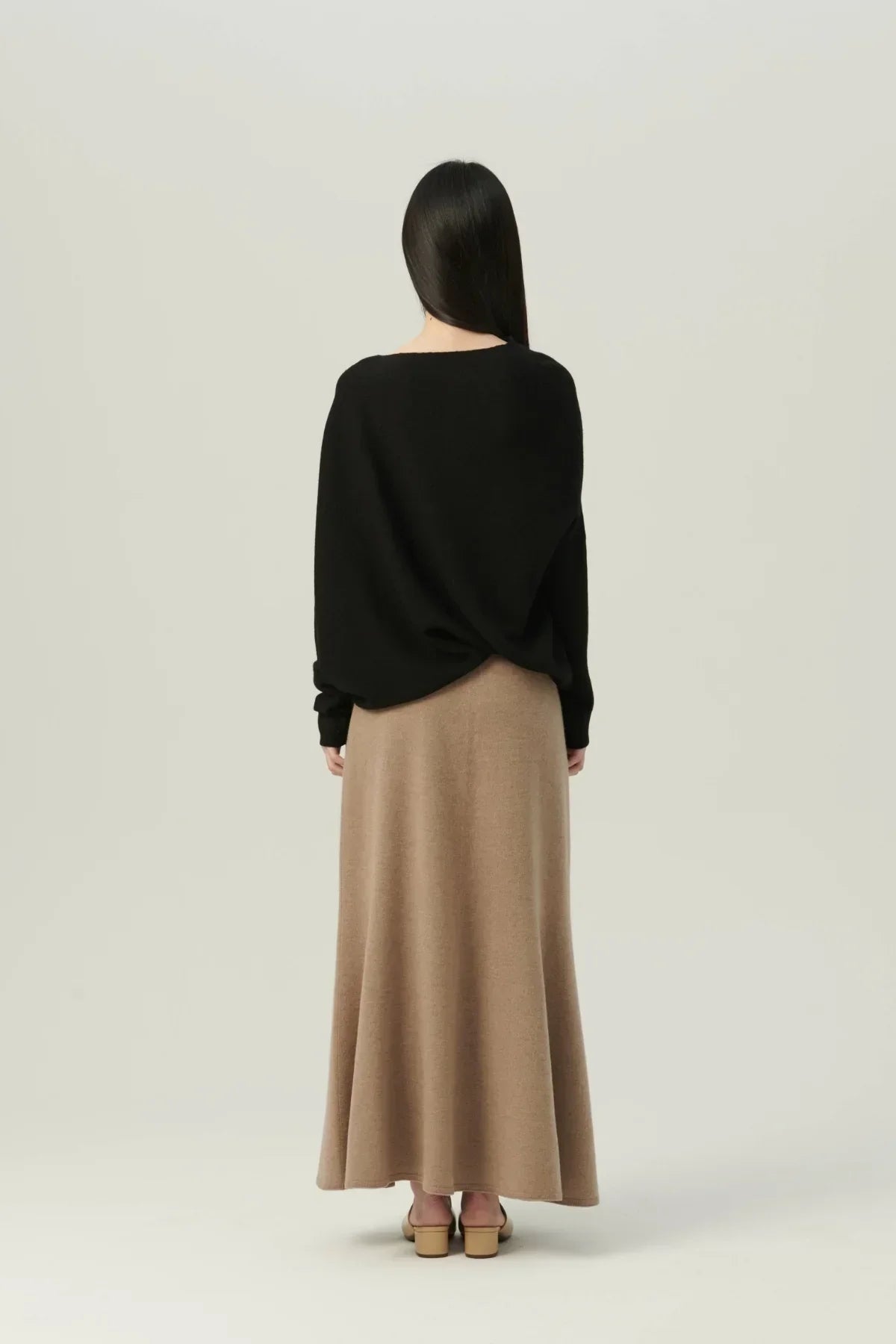 Woman in a black oversized sweater and beige maxi skirt standing against plain background