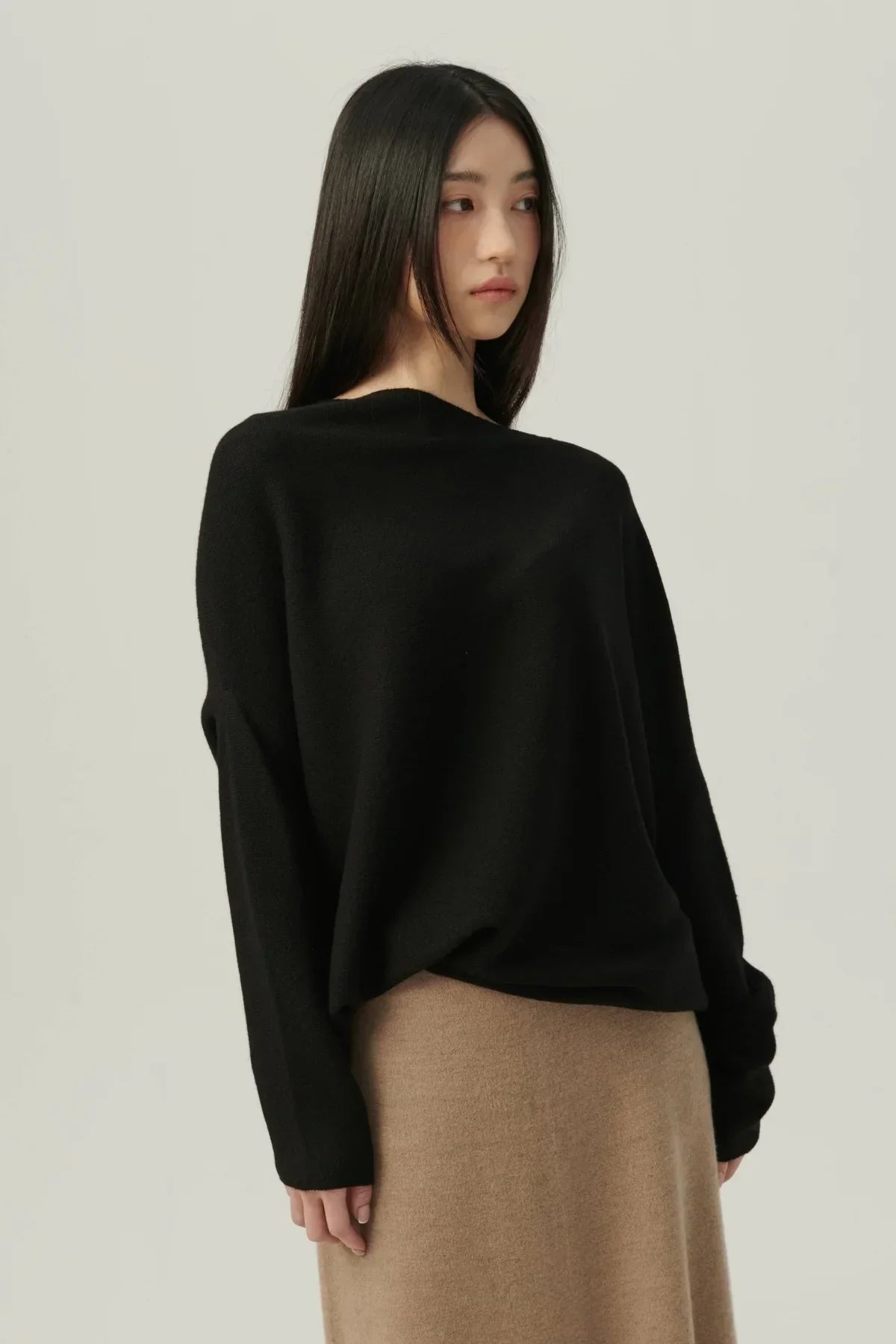 Woman wearing black oversized knit sweater and beige skirt on light background