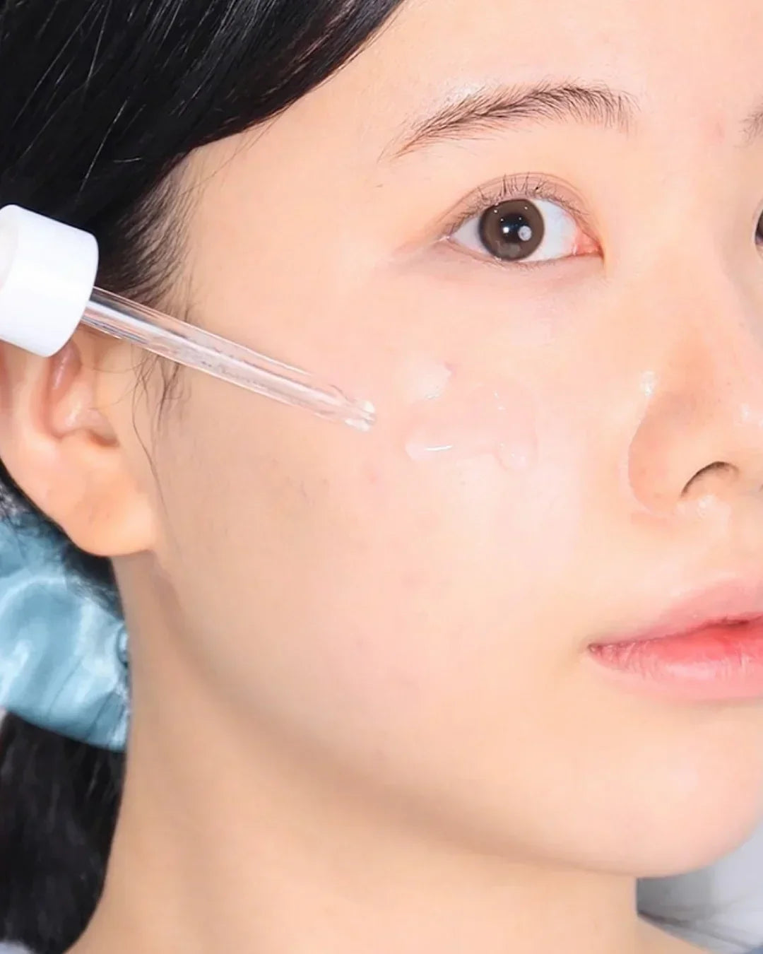Close-up of woman applying clear serum with dropper on cheek for skincare