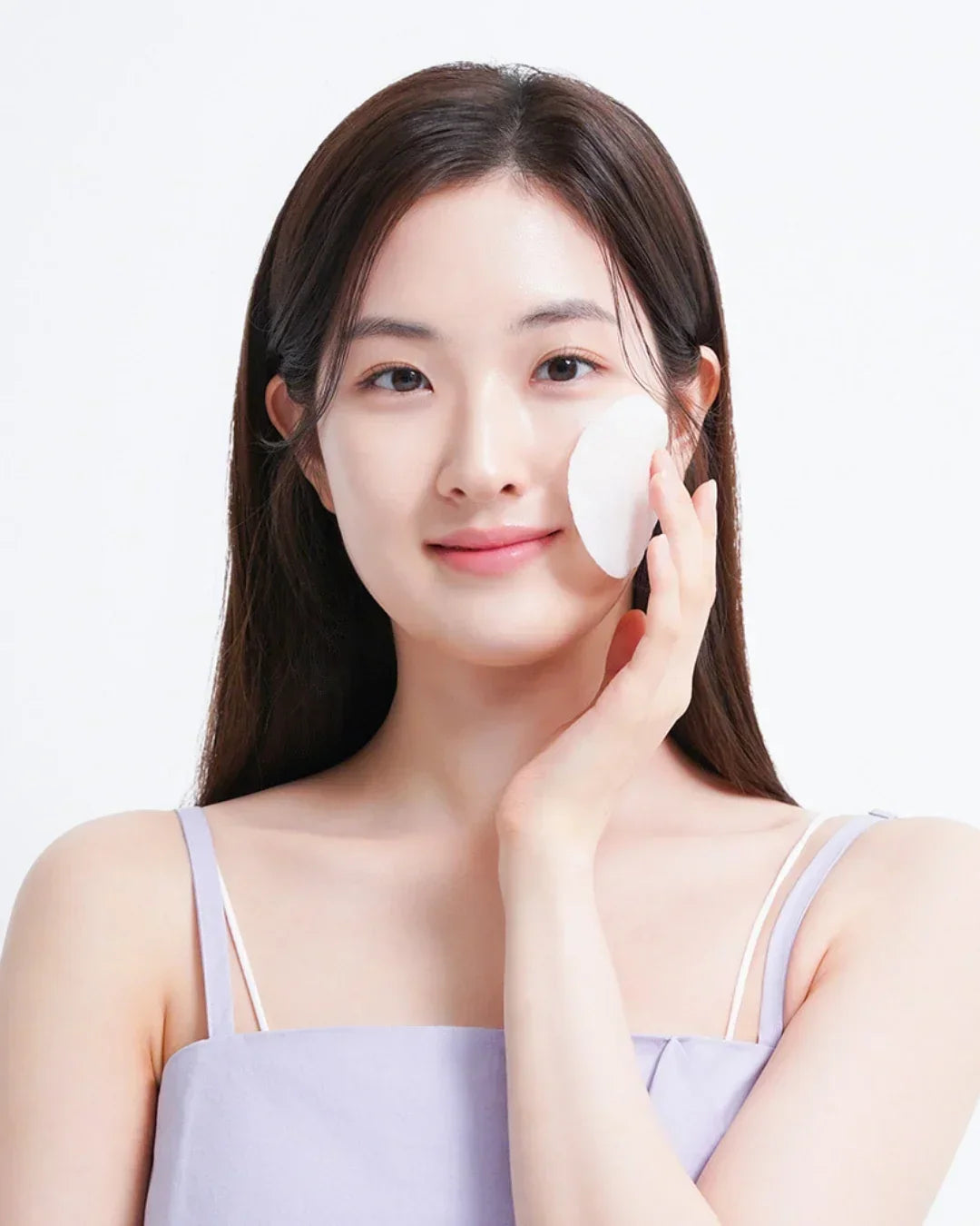 Young woman with clear skin using a white cleansing cotton pad on her face, skincare routine