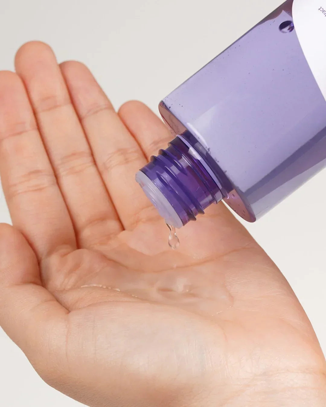 Hand pouring clear essence toner liquid from a purple bottle onto palm, skincare application