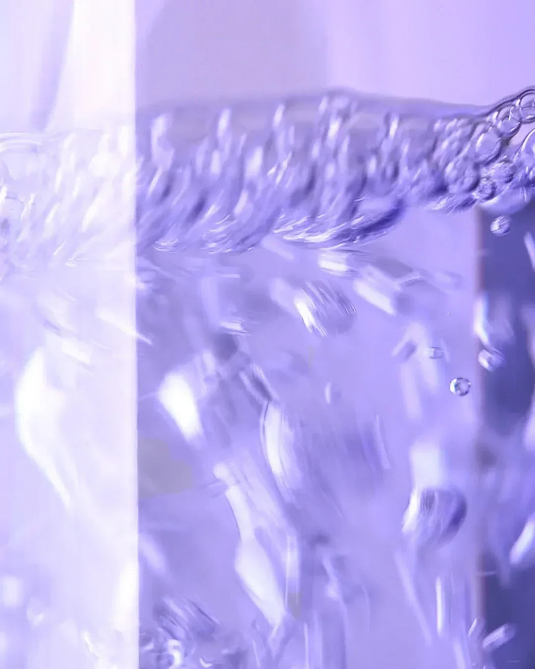 Close-up of clear liquid bubbles inside a skincare toner bottle with purple lighting