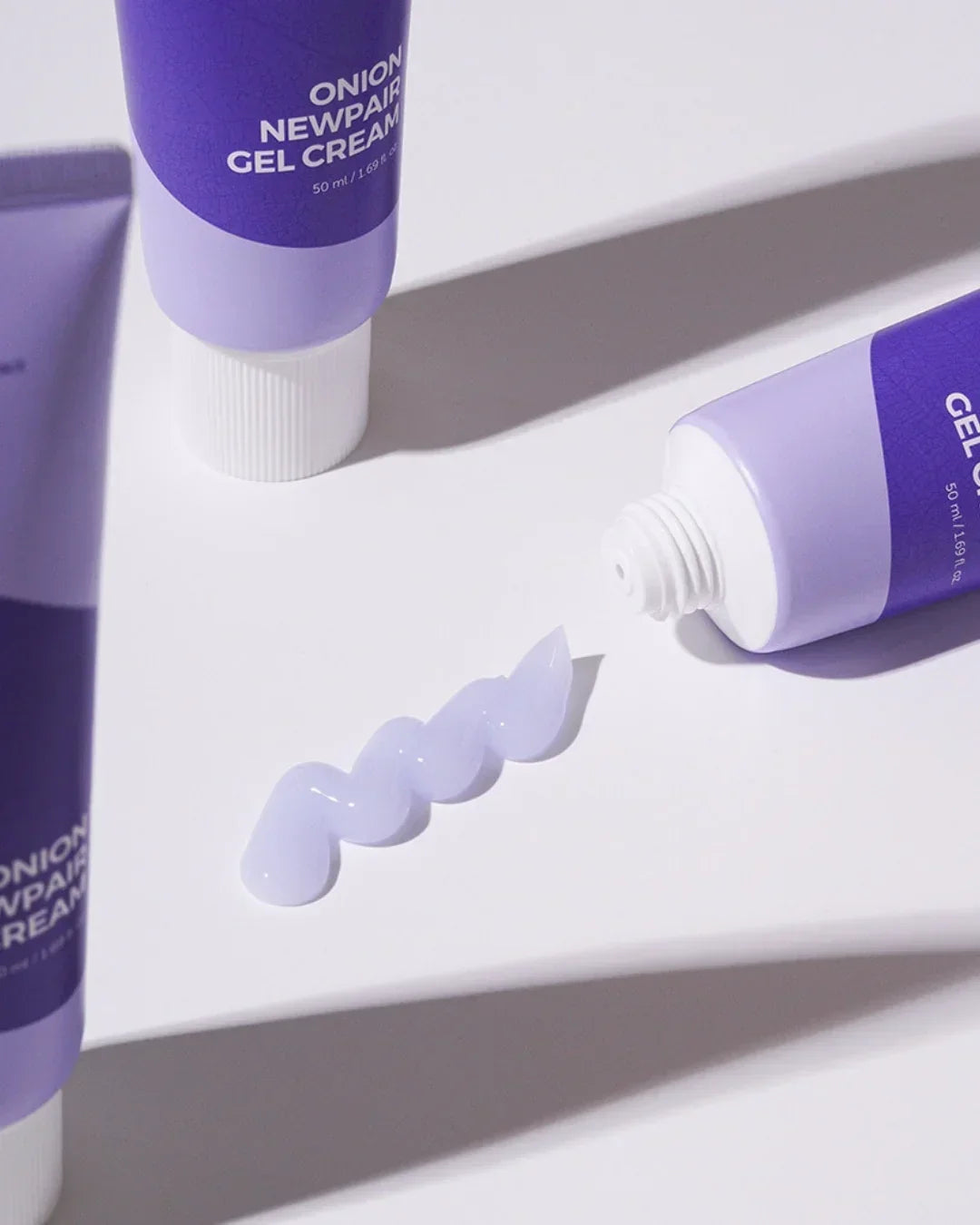Purple tubes of Onion Newpair Gel Cream with cream squeezed out on white surface