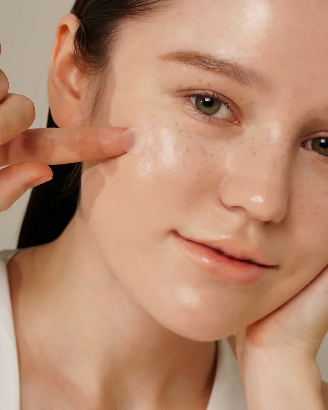 Close-up of woman applying small translucent skincare spot patch on cheek with clear skin and freckles