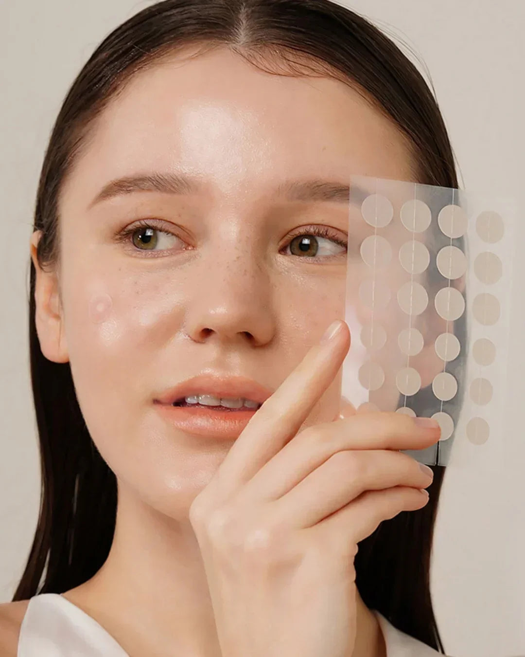Woman with clear skin holding translucent acne spot patches near her cheek