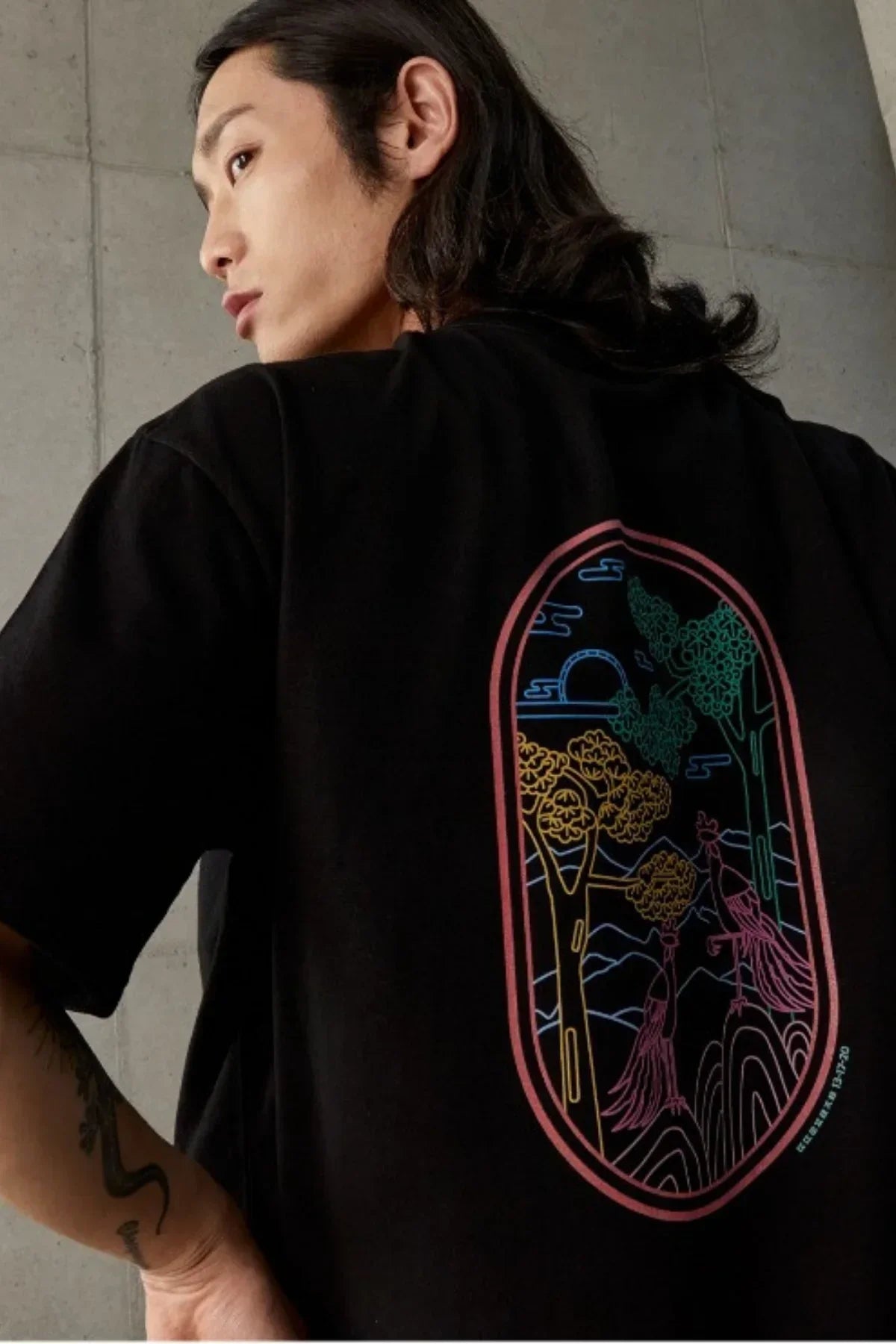 Black t-shirt with colorful neon line art of two birds and trees on back, worn by model indoors