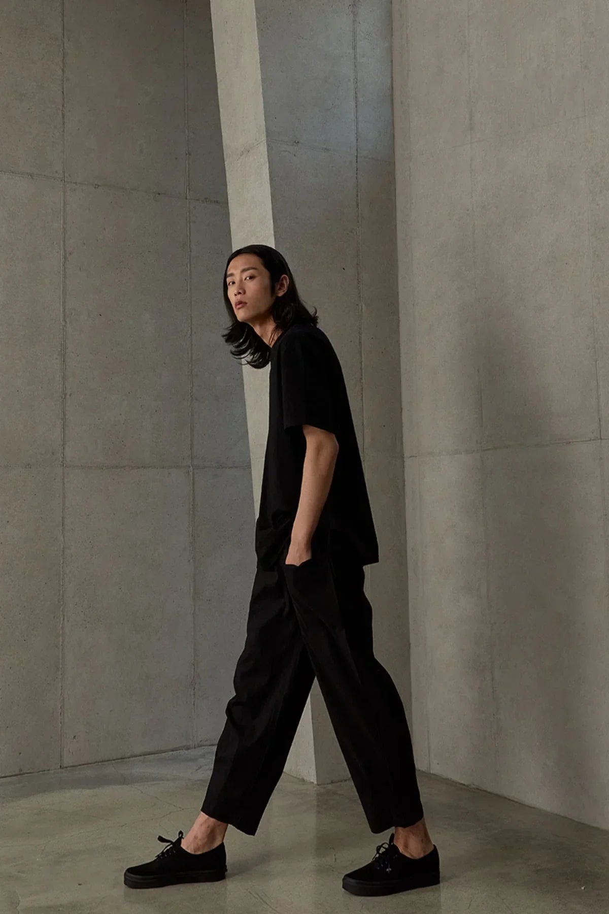 Man wearing black t-shirt and pants walking in minimalist concrete architectural setting