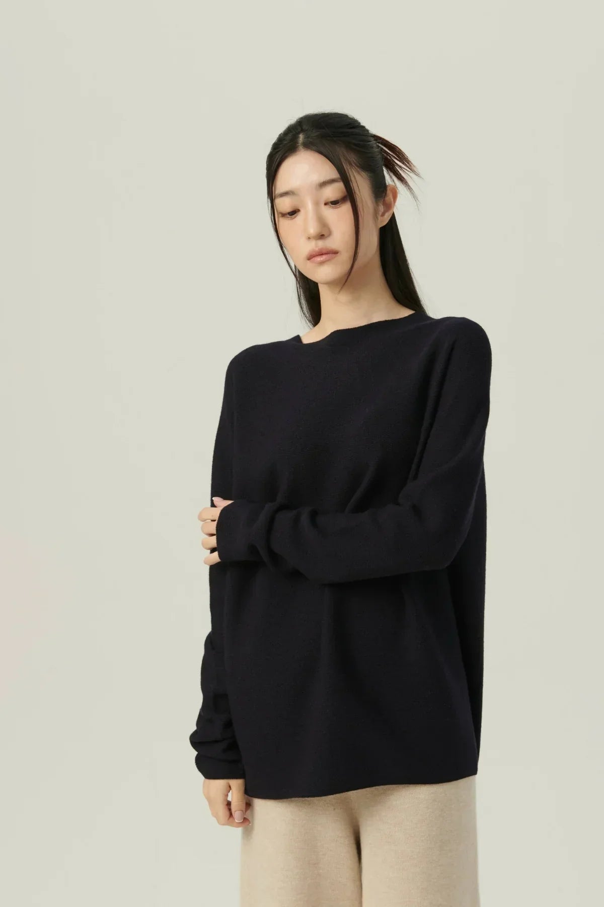 Woman wearing oversized black sweater and beige pants against a plain light background