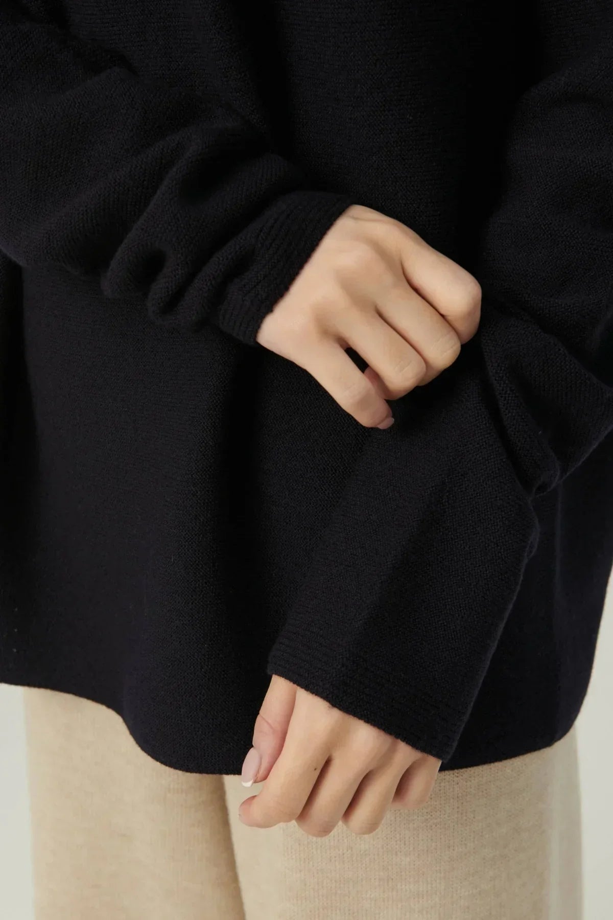 Close-up of hands wearing a black knit pullover with ribbed cuffs over beige pants