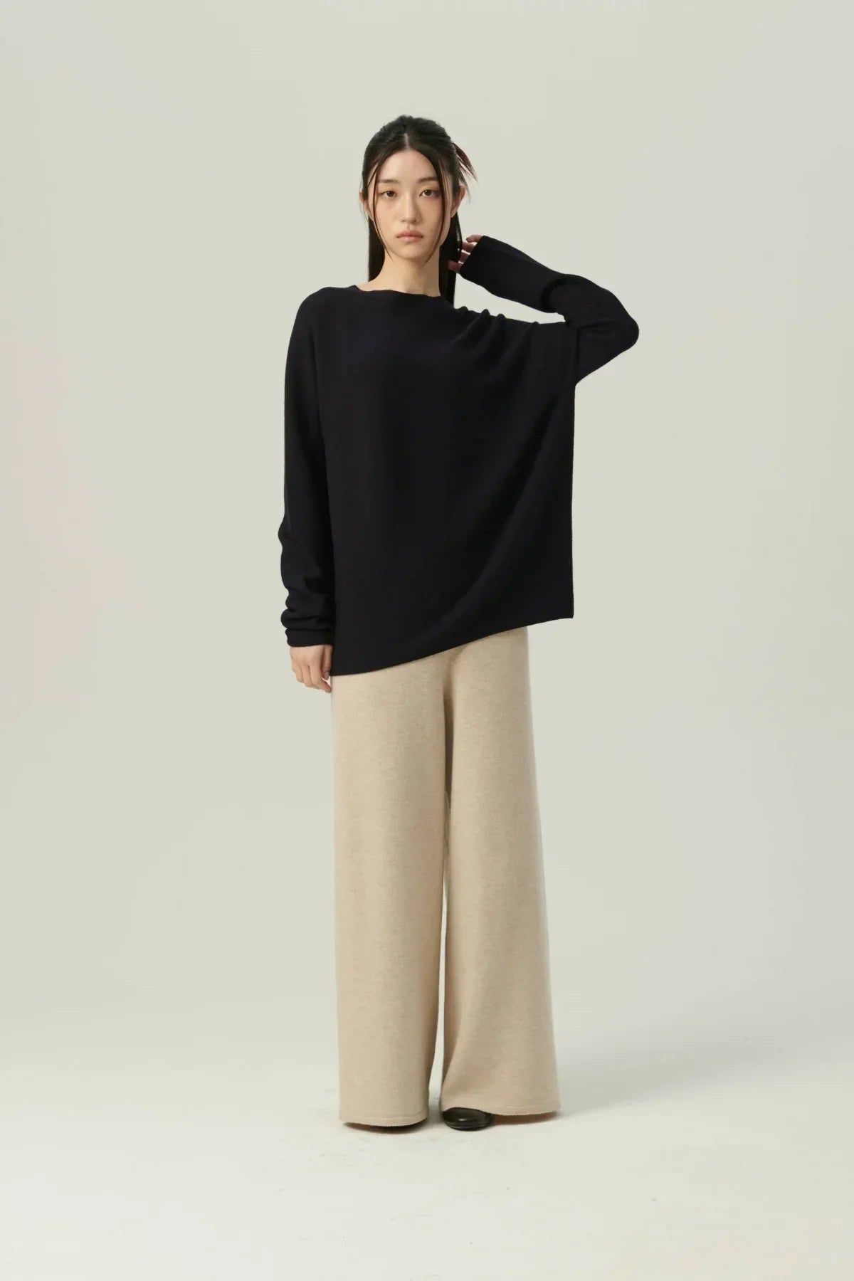 Woman wearing navy oversized knit pullover and beige wide-leg pants on plain background