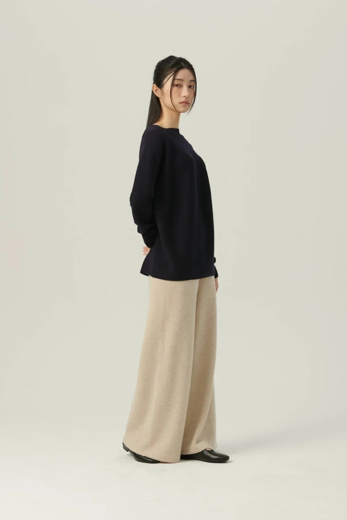 Young woman wearing navy knit pullover and wide beige pants in a studio with light background