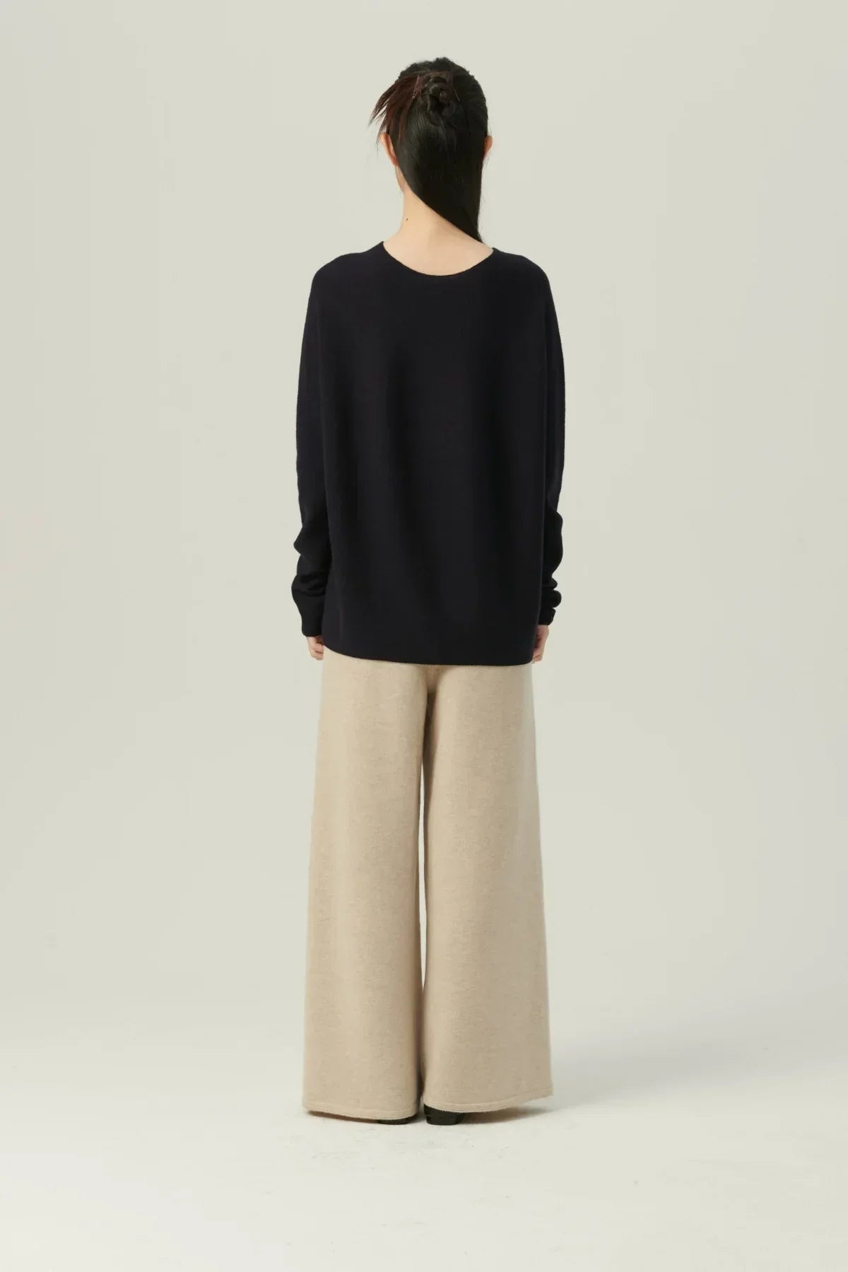 Woman wearing navy oversized sweater and beige wide-leg pants standing against light background