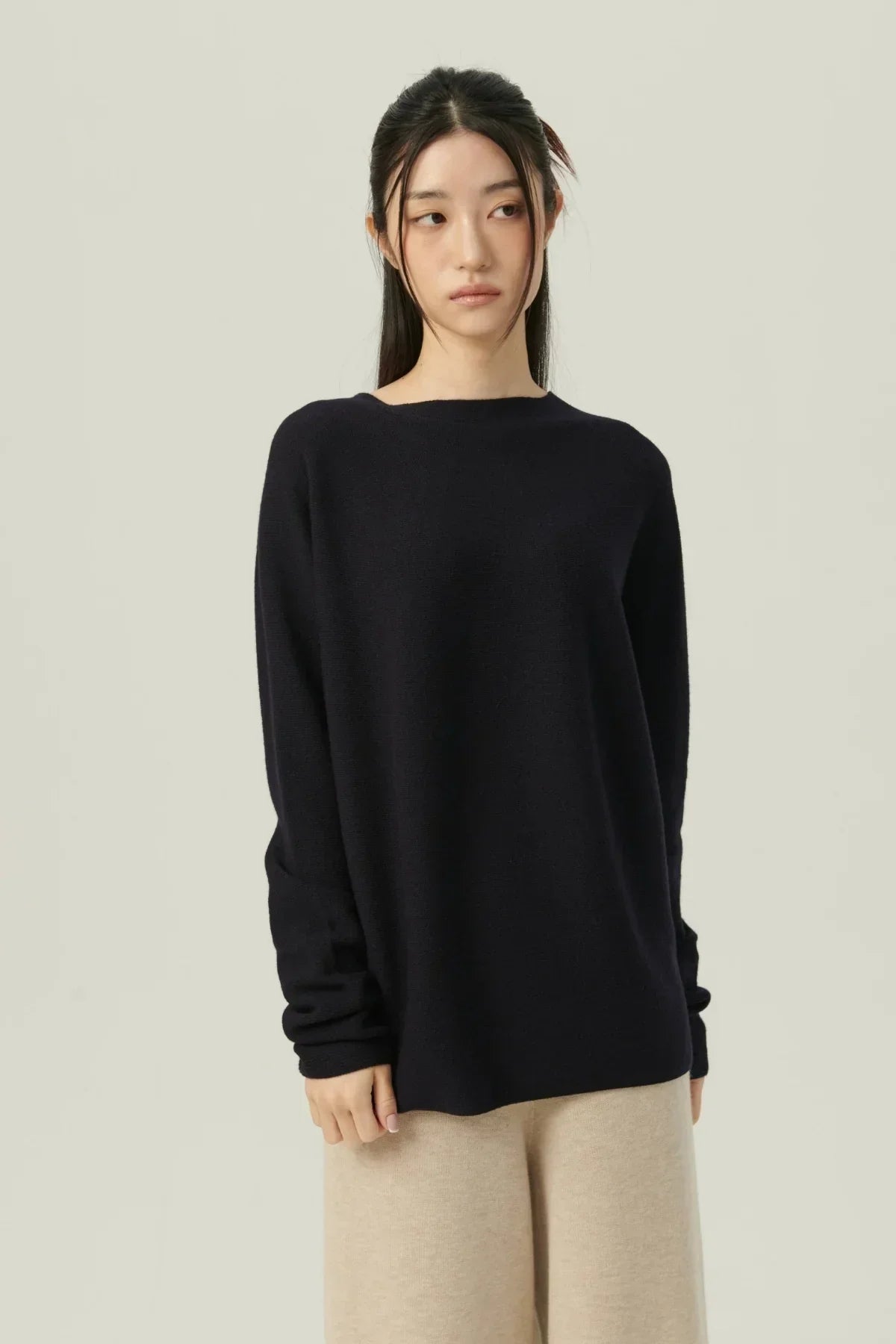 Young woman wearing a navy navy pullover sweater and beige pants against a plain background