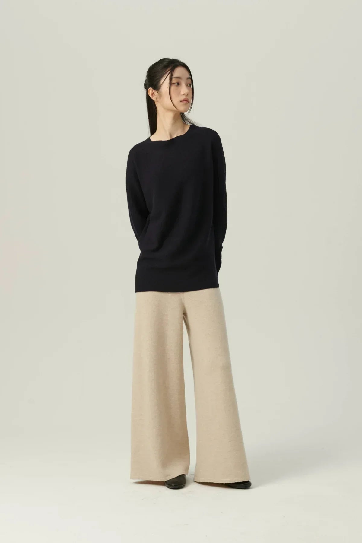 Model wearing navy knit pullover with beige wide-leg pants on plain background
