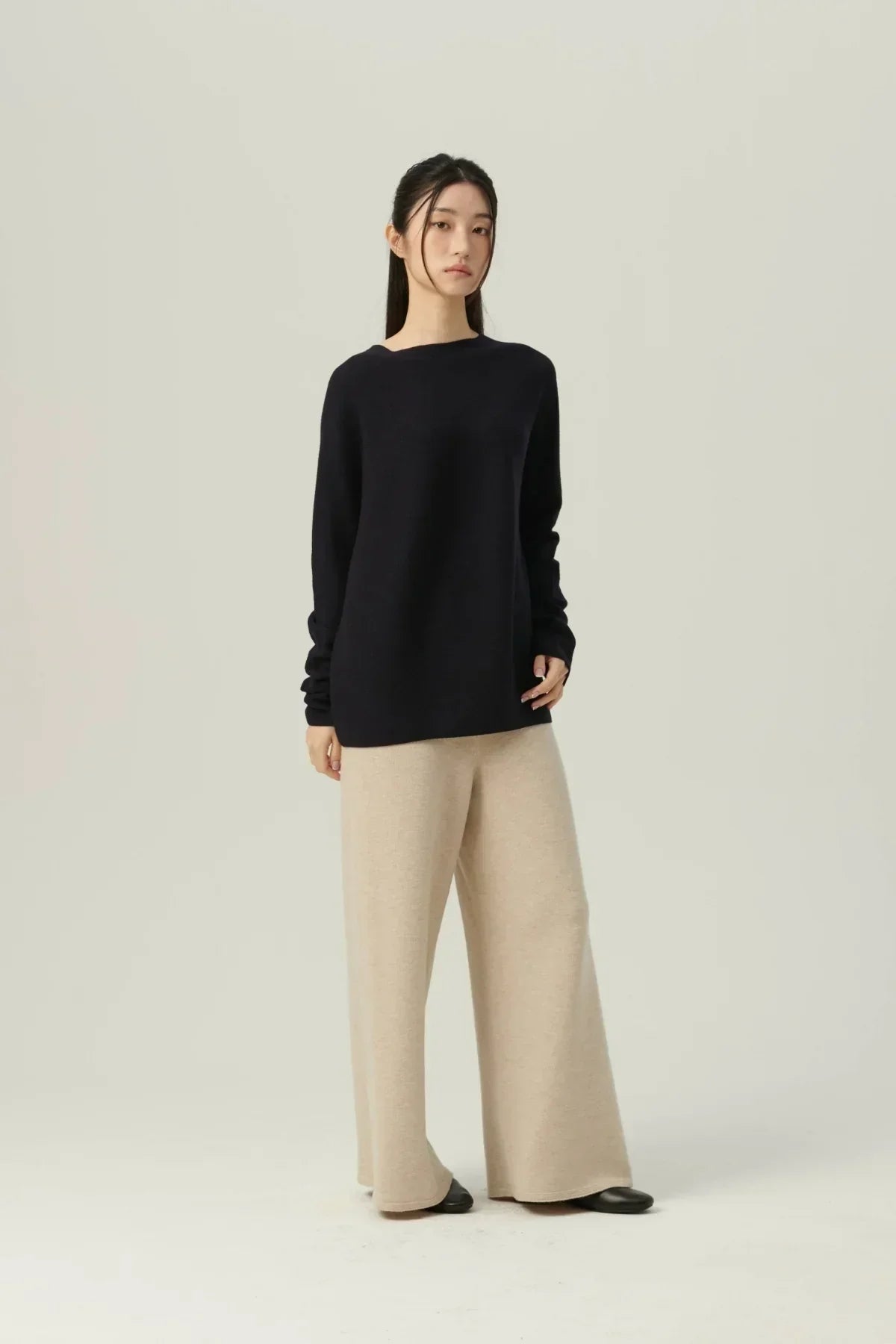 Woman in navy knit pullover and beige wide-leg pants standing against plain background
