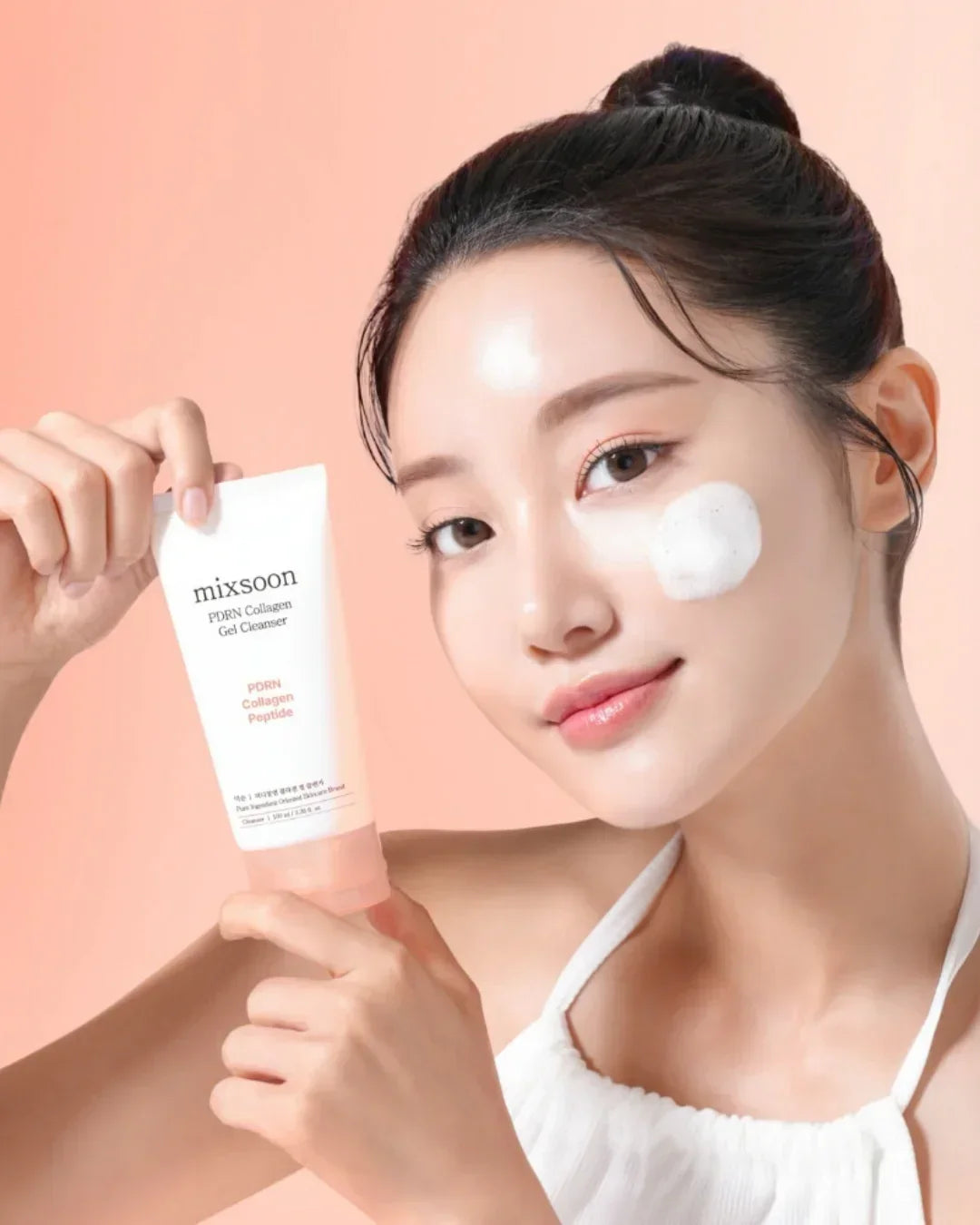 Young woman with clear skin holding Mixsoon PDRN Collagen Gel Cleanser with foam on cheek