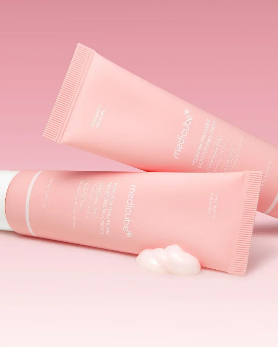 Two pink Medicube PDRN Pink Hyaluronic Moisturizing Cream tubes on pink background with cream texture