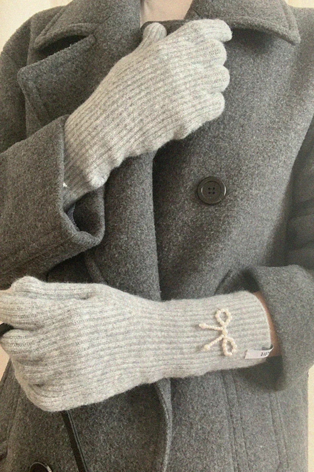 Person wearing gray ribbed knit gloves with pearl ribbon detail and matching gray wool coat