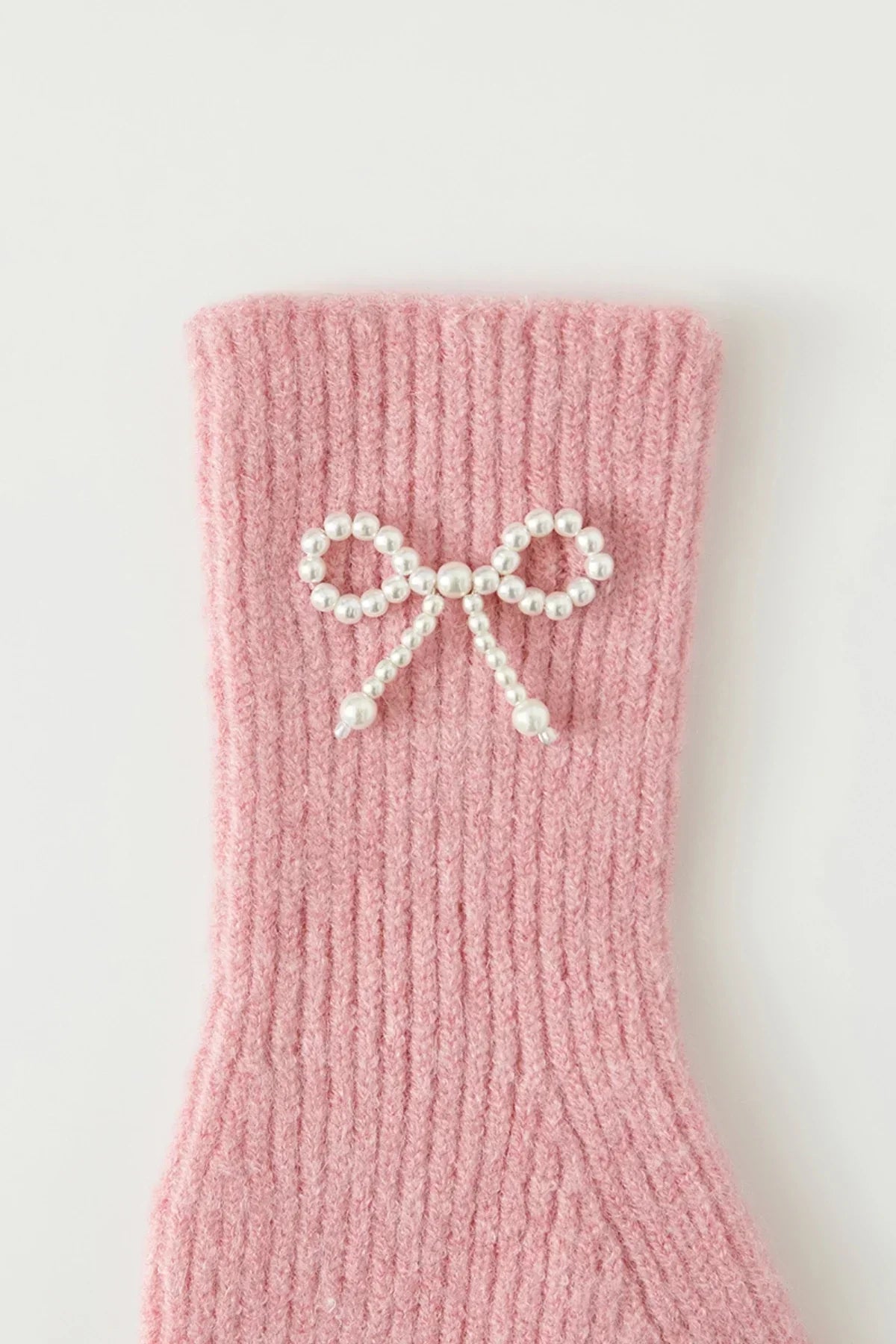 Pink knitted fabric with a decorative bow made of white pearls on a white background
