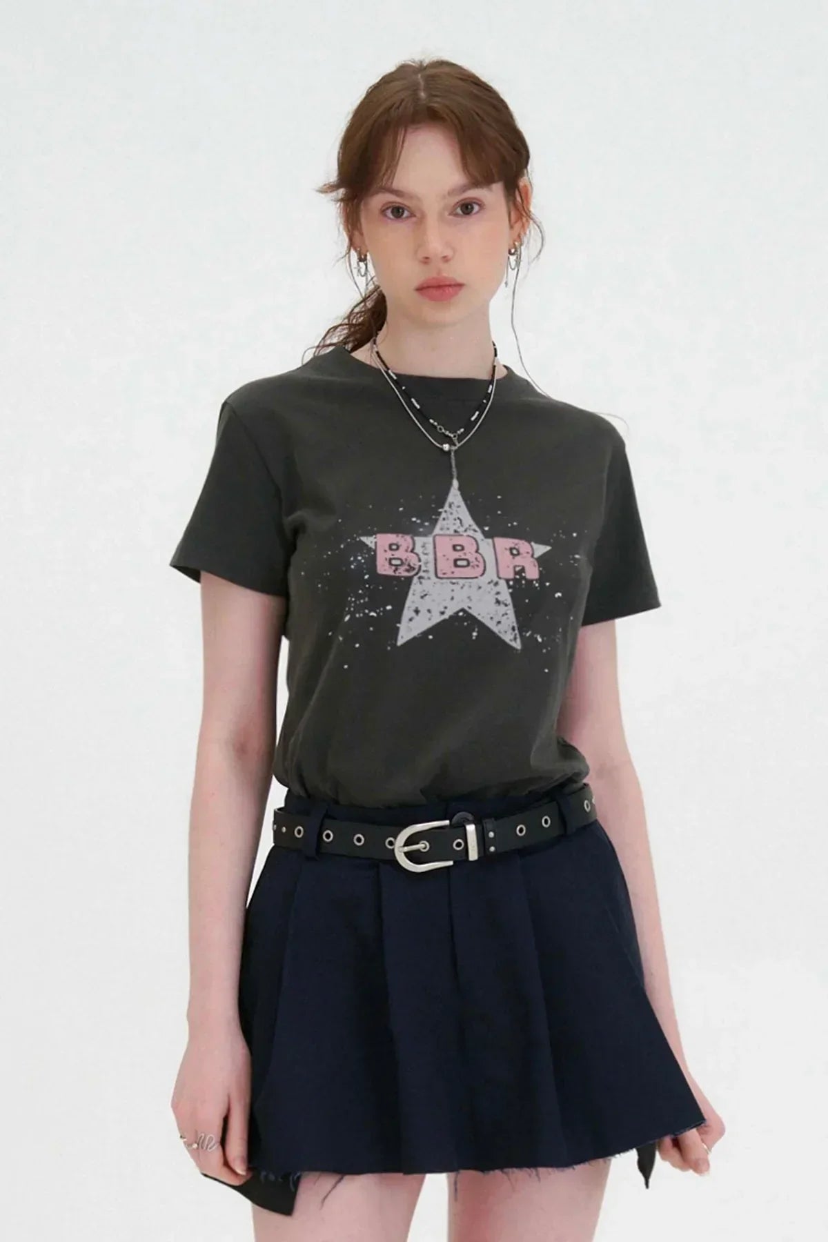Young woman wearing charcoal t-shirt with pink BBR letters and star print, navy pleated skirt with black belt