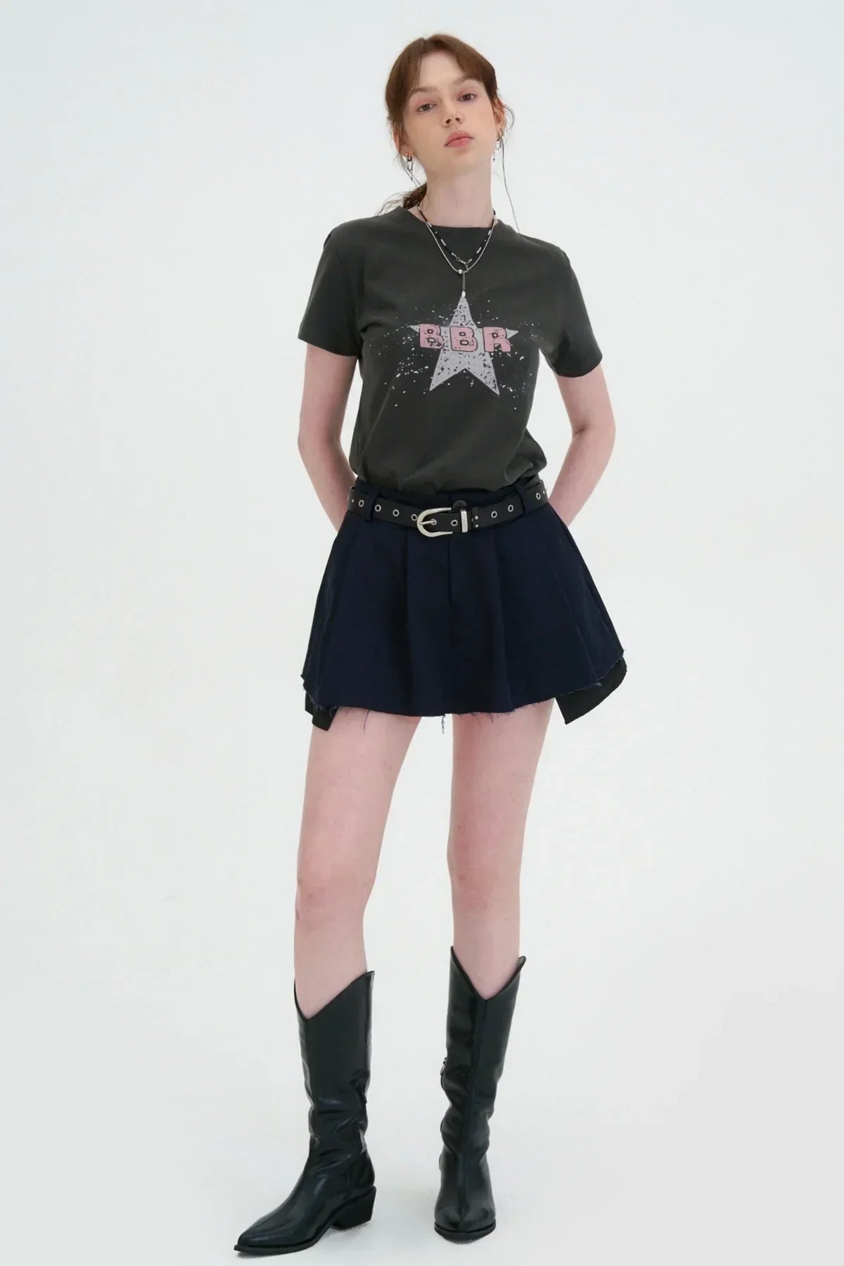 Woman wearing charcoal graphic t-shirt with star and BBR print, black pleated mini skirt, and black boots