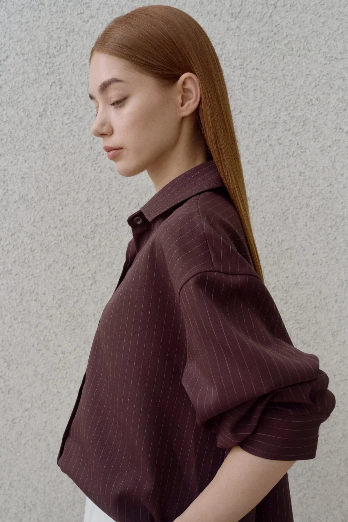 Side profile of woman with straight hair wearing brown pinstripe shirt with rolled sleeves