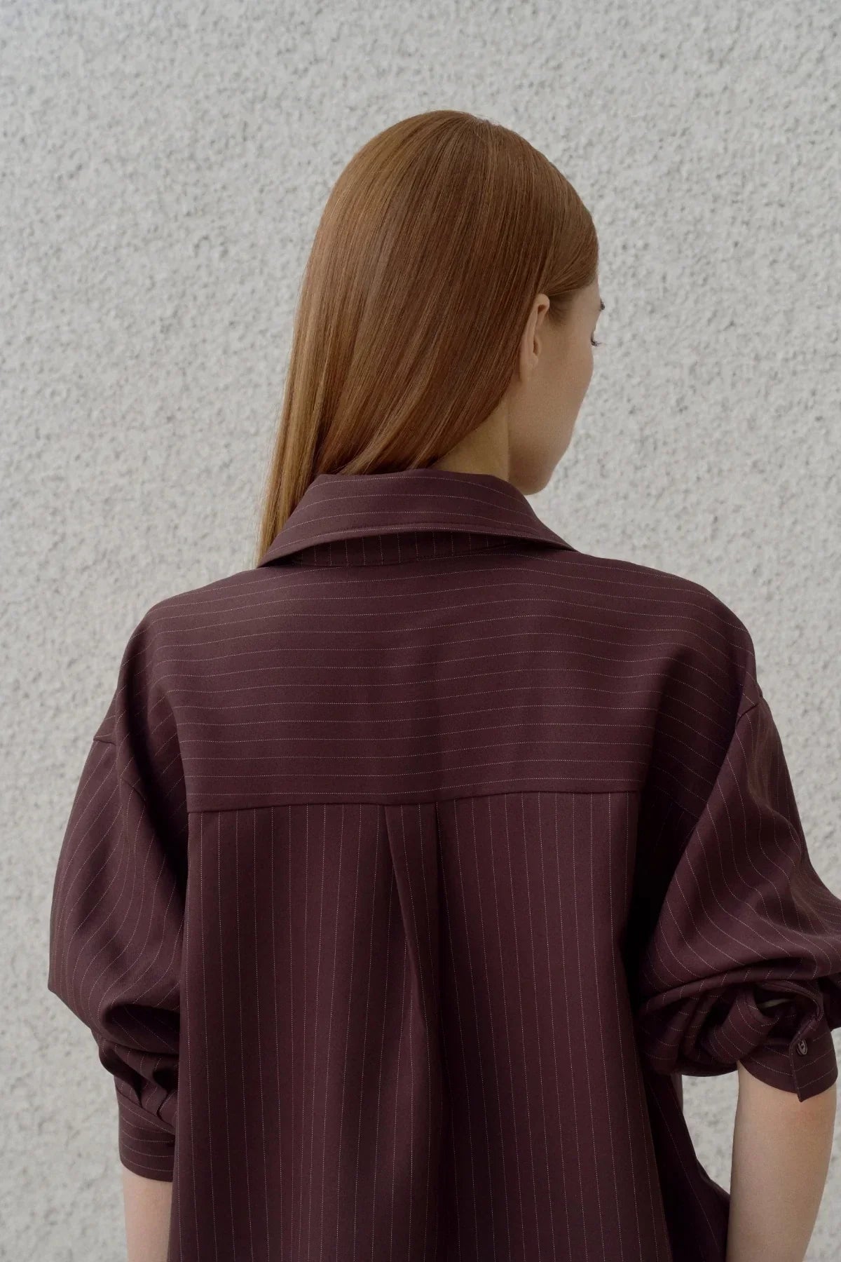 Back view of woman with straight chestnut hair wearing brown pinstripe shirt with rolled sleeves
